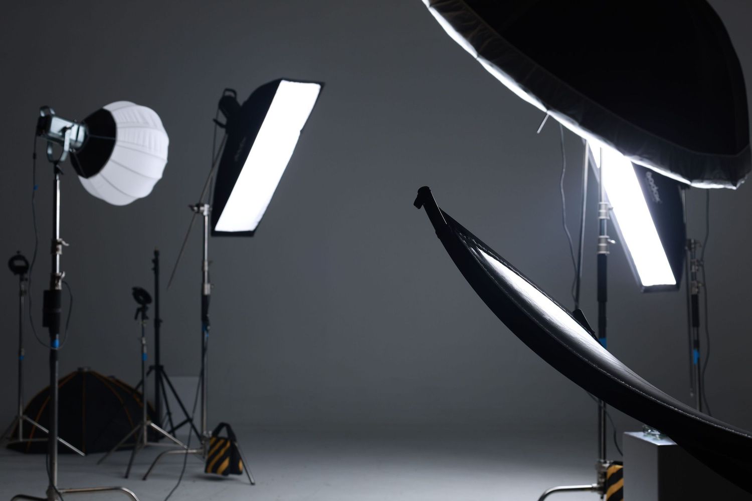 Professional photography studio with multiple softbox lights, reflectors, and light stands set up on a gray backdrop.