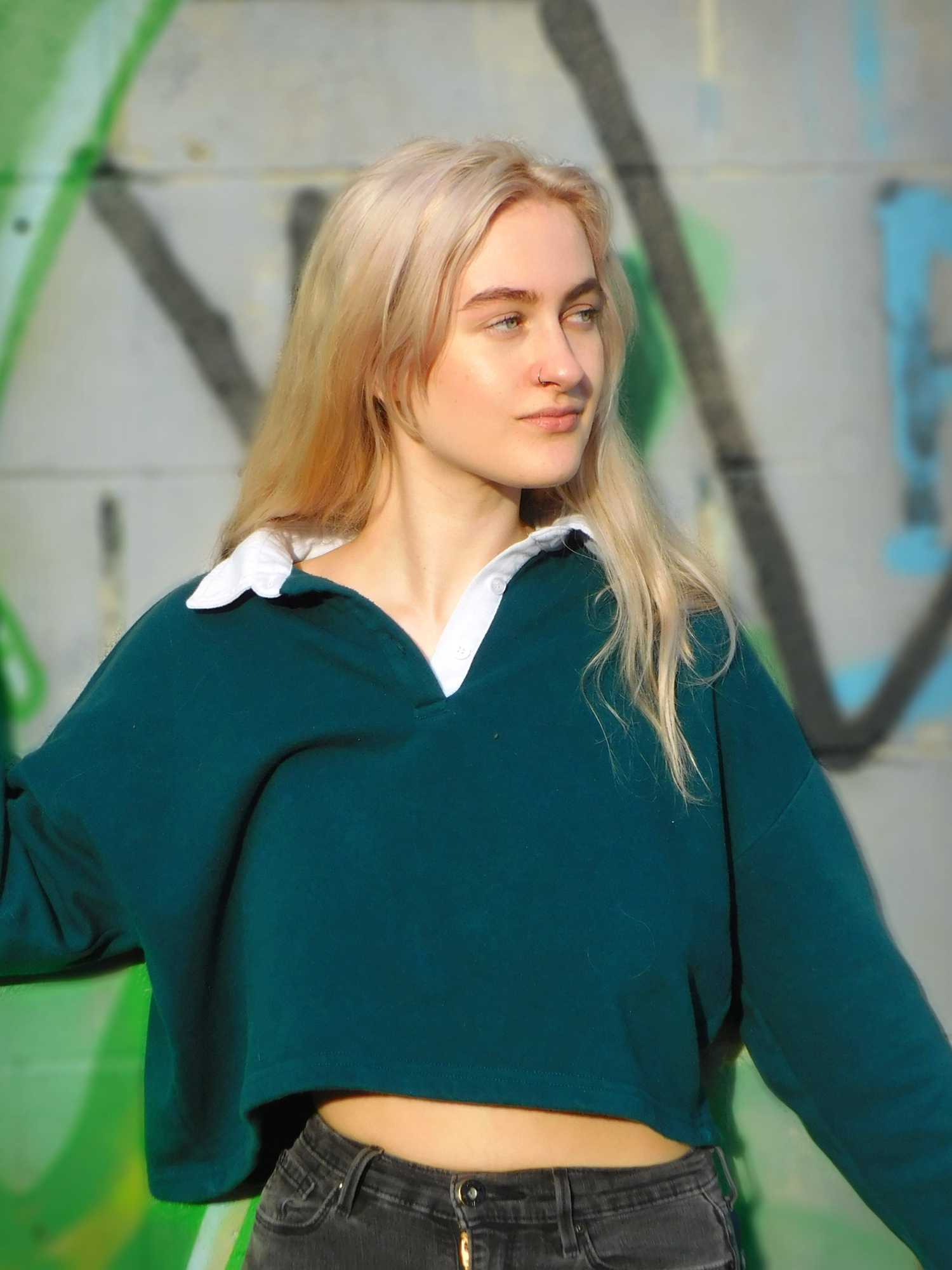 Casual street style look featuring a cropped green sweater against graffiti wall.