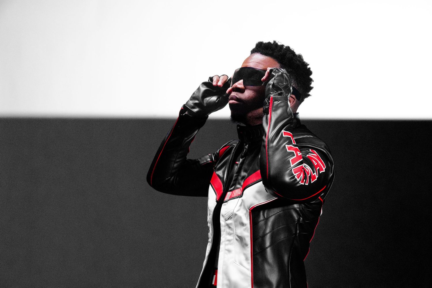A performer in a black leather jacket sings into a microphone on stage under dramatic lighting.