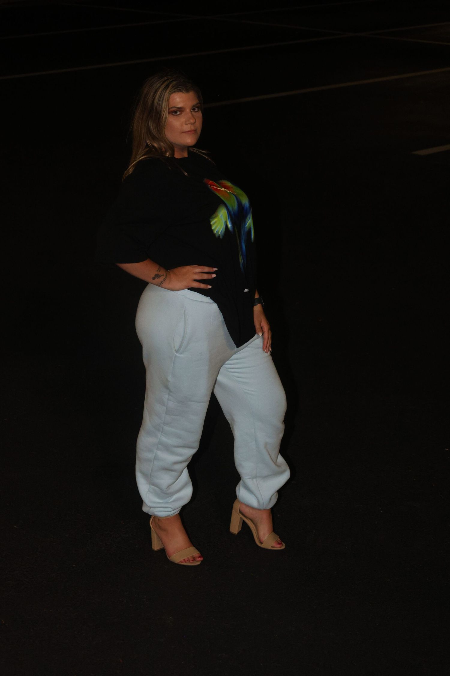 Fashion portrait of someone wearing white joggers and a dark top with colorful details in night setting.