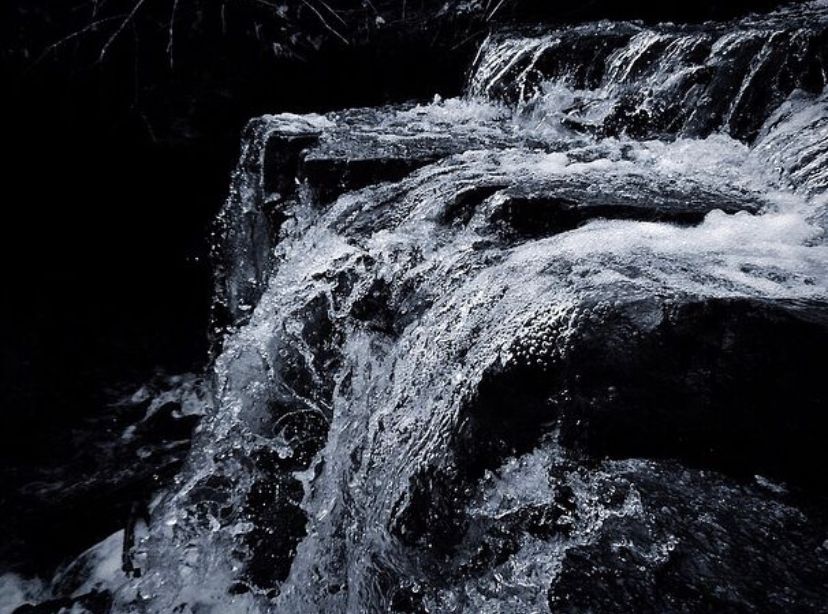 A dramatic black and white waterfall cascades over dark rocks, with white foamy water rushing powerfully downstream.