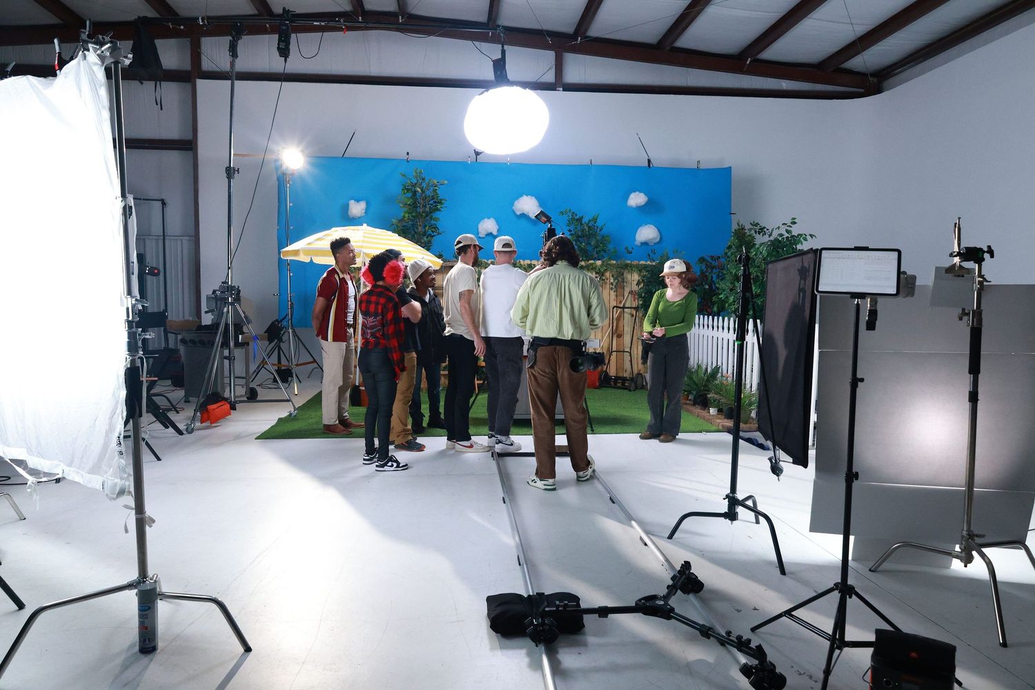 Group of people standing in a photography studio with colorful backdrop, lighting equipment, and props during a photo shoot.