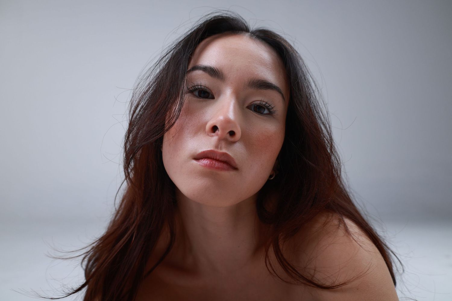 Close-up portrait of a young woman with long dark hair against a soft gray background.