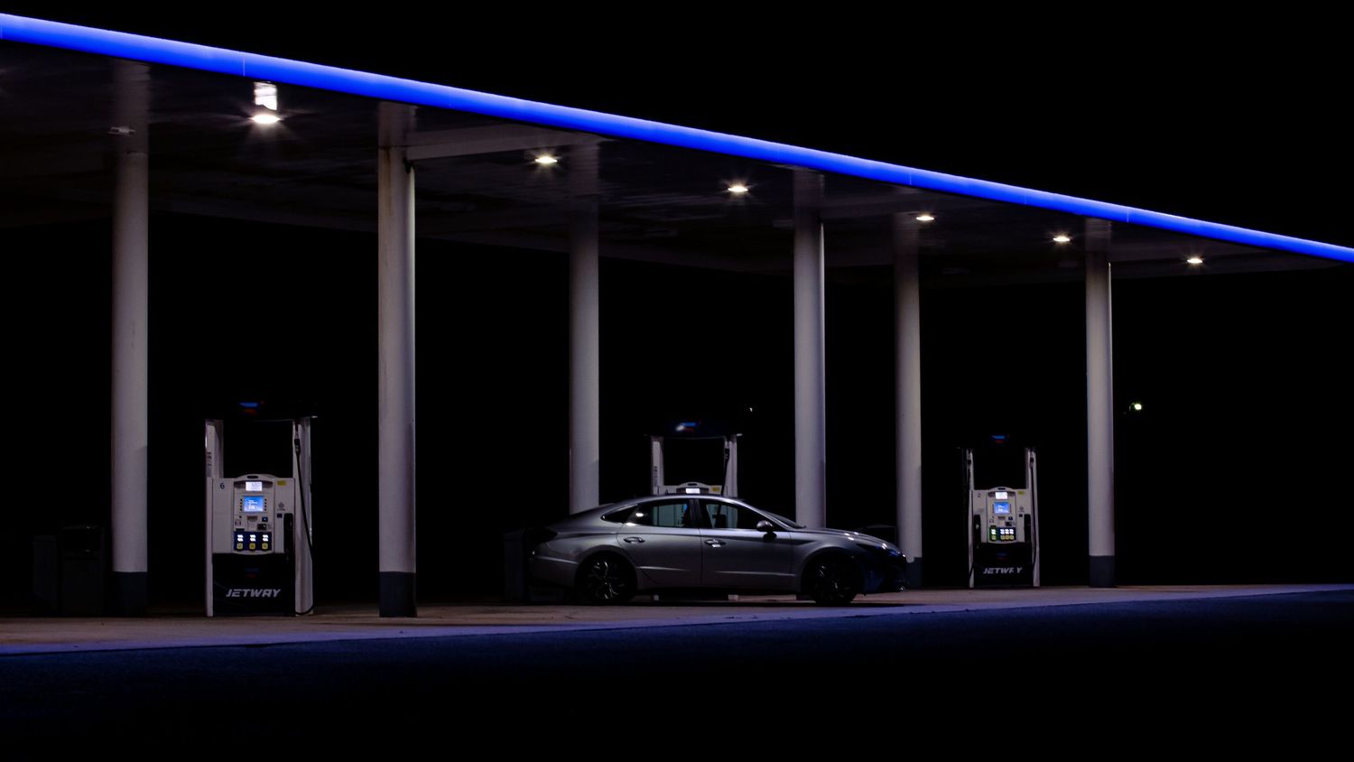 Car at illuminated gas station at night with blue LED lights.