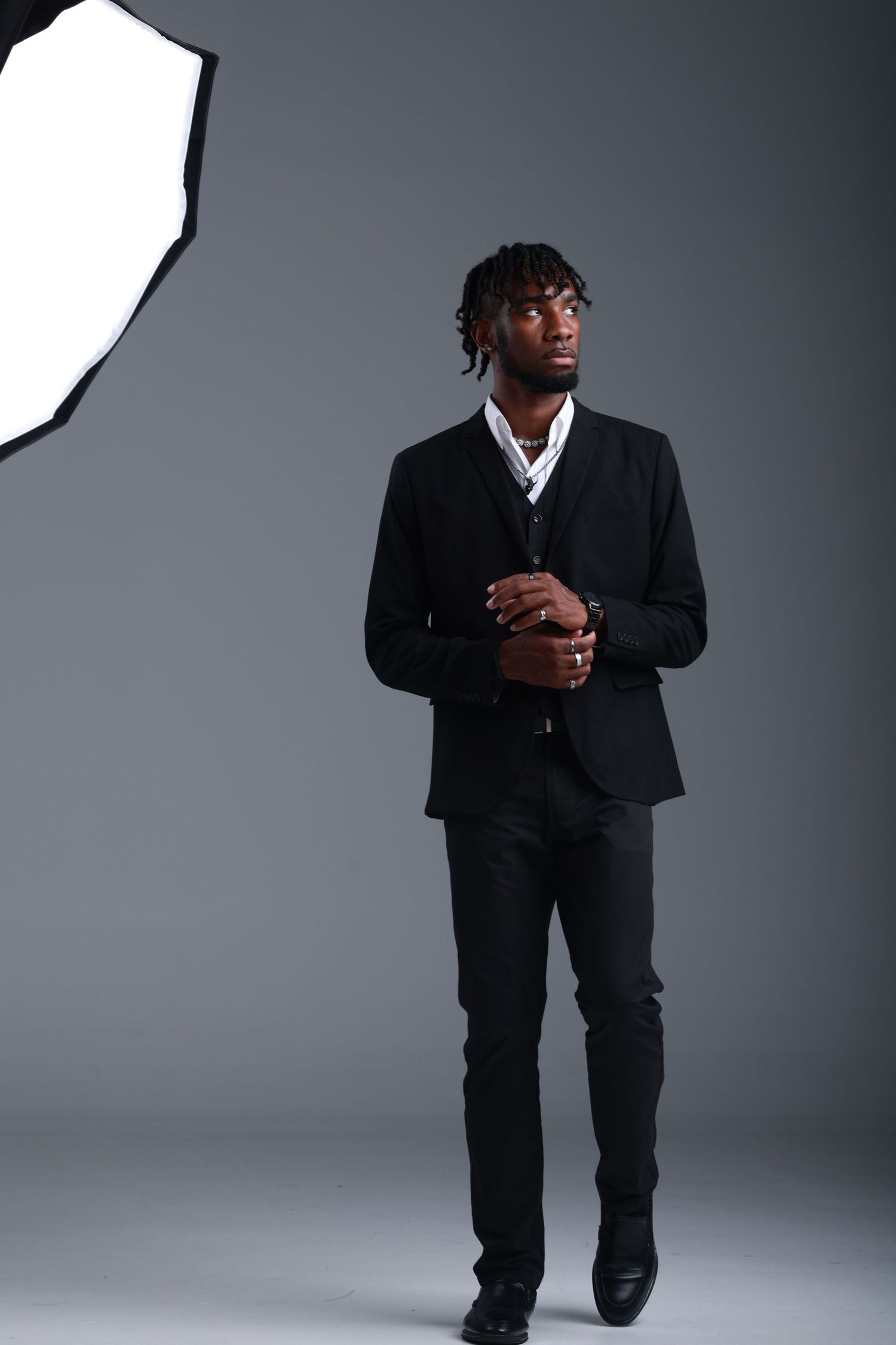 Young Black man in black suit with white shirt poses confidently in professional photo studio with softbox lighting.