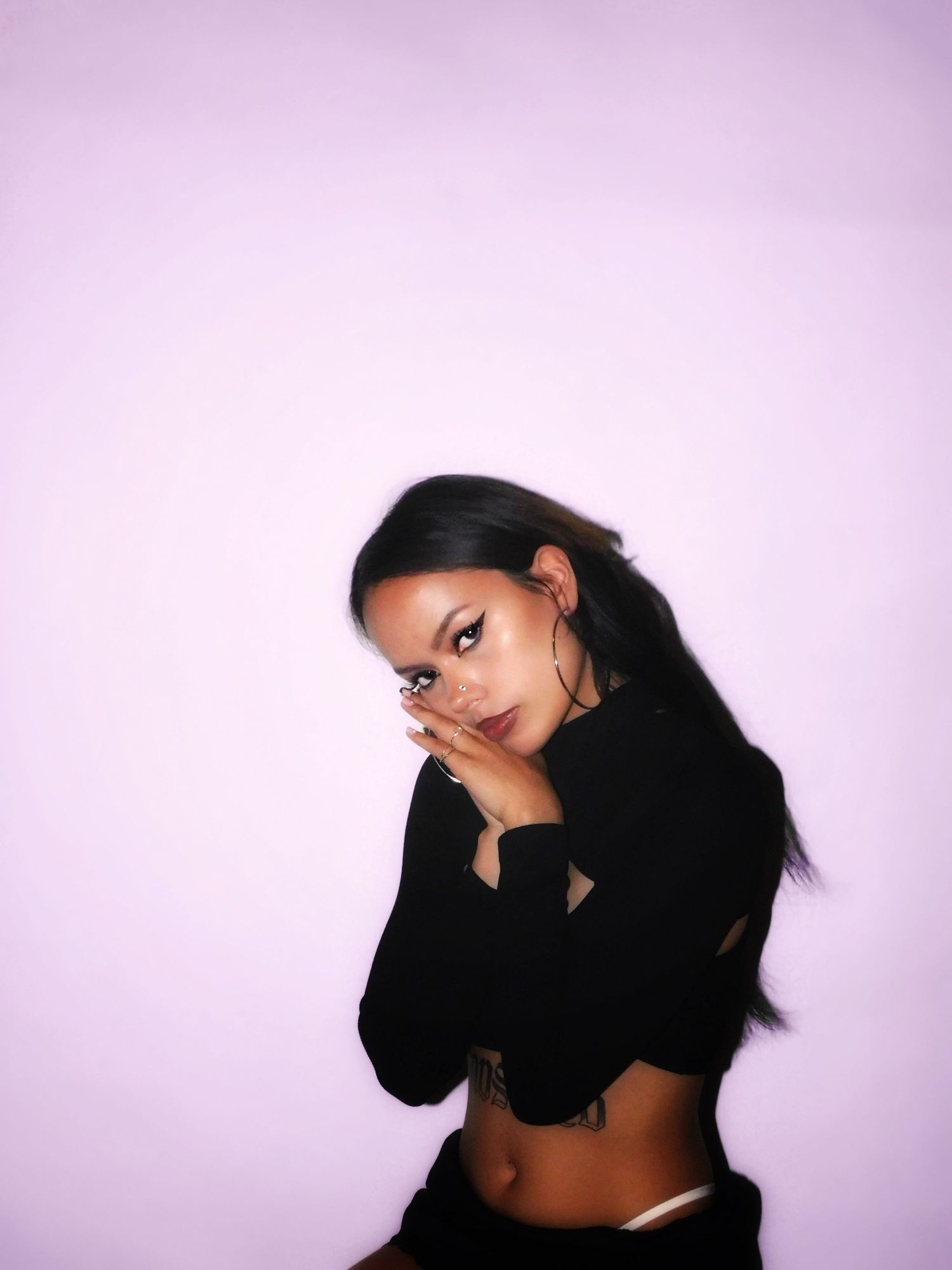 Young woman in black crop top posing against purple background.