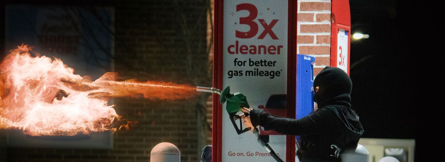 A person in tactical gear confronts flames and fire during an intense urban conflict situation.