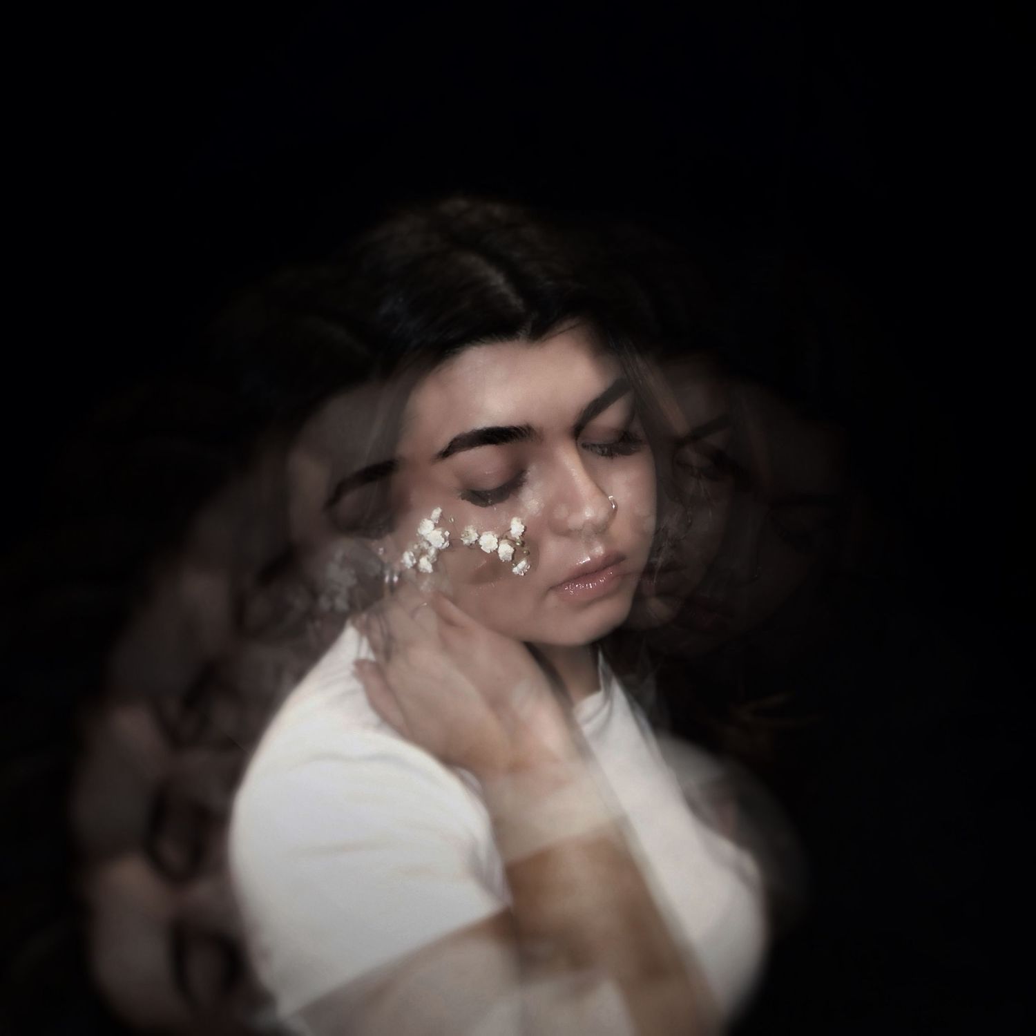 A woman with dark hair poses with eyes closed, adorned with floral accessories, in a dreamy double-exposure portrait.