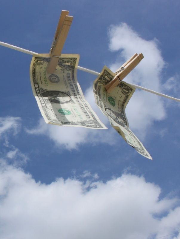Dollar bills hanging from a clothesline against blue sky with white puffy clouds.