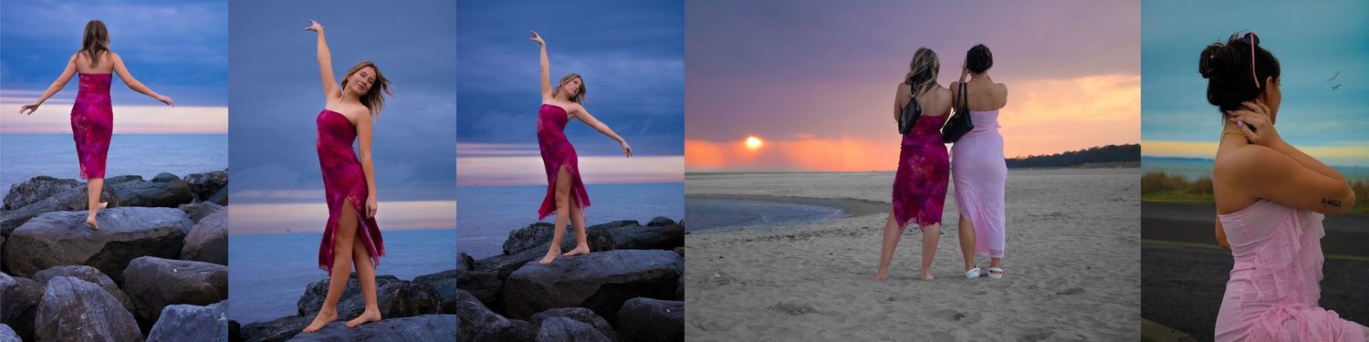 Woman in pink dress poses on rocks by ocean at sunset, arms raised joyfully against colorful sky.