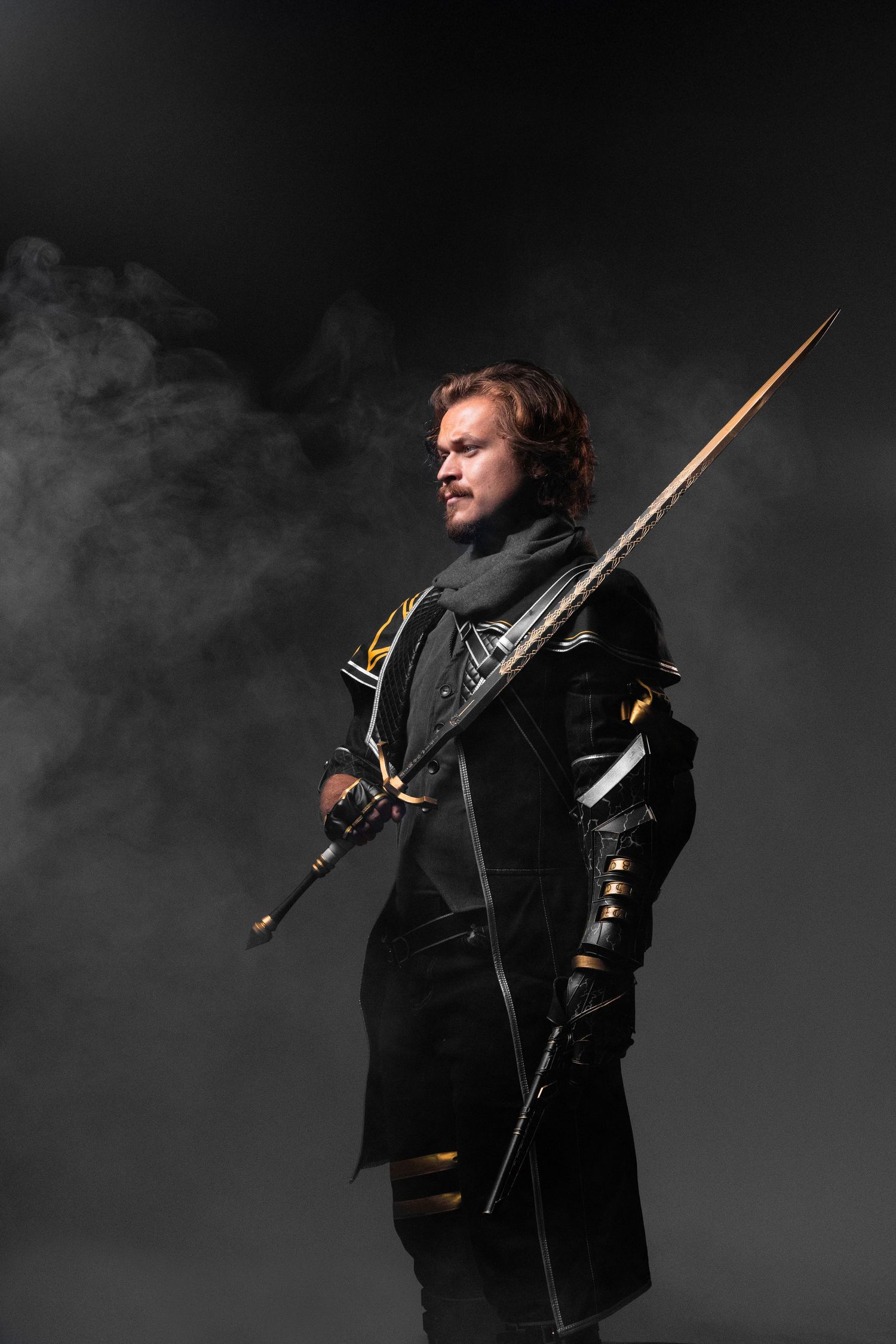A medieval knight in black armor holds a long sword against a dramatic smoky dark background.