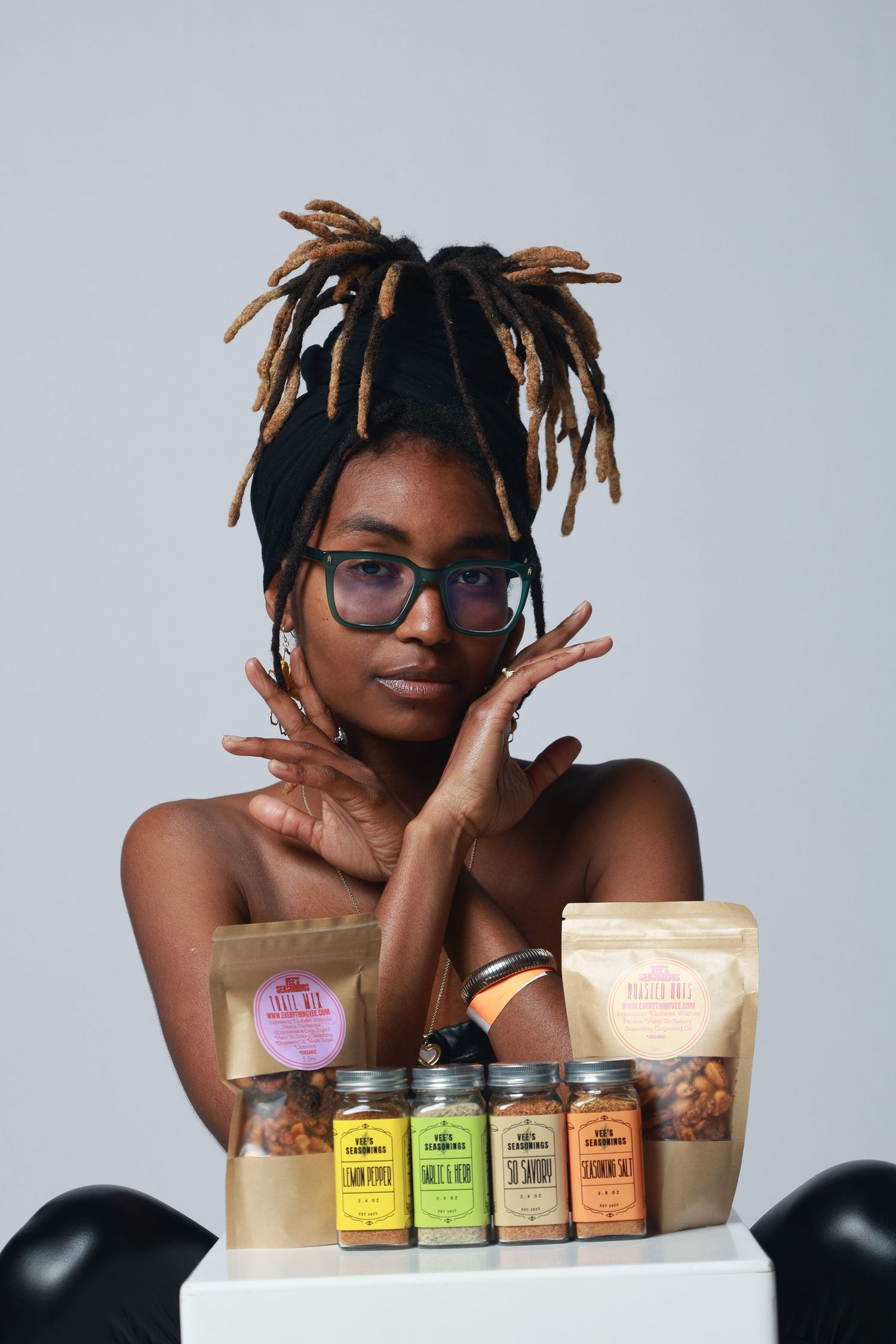 Young woman with dreadlocks and glasses posing with artisan spice jars and kraft packaging products.