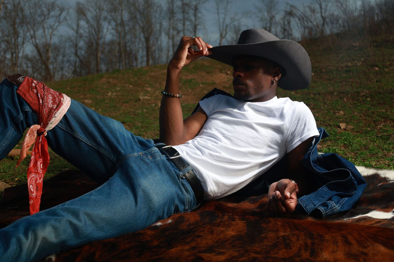 A man in a cowboy hat and white t-shirt relaxes on a horse, wearing jeans and a red bandana.