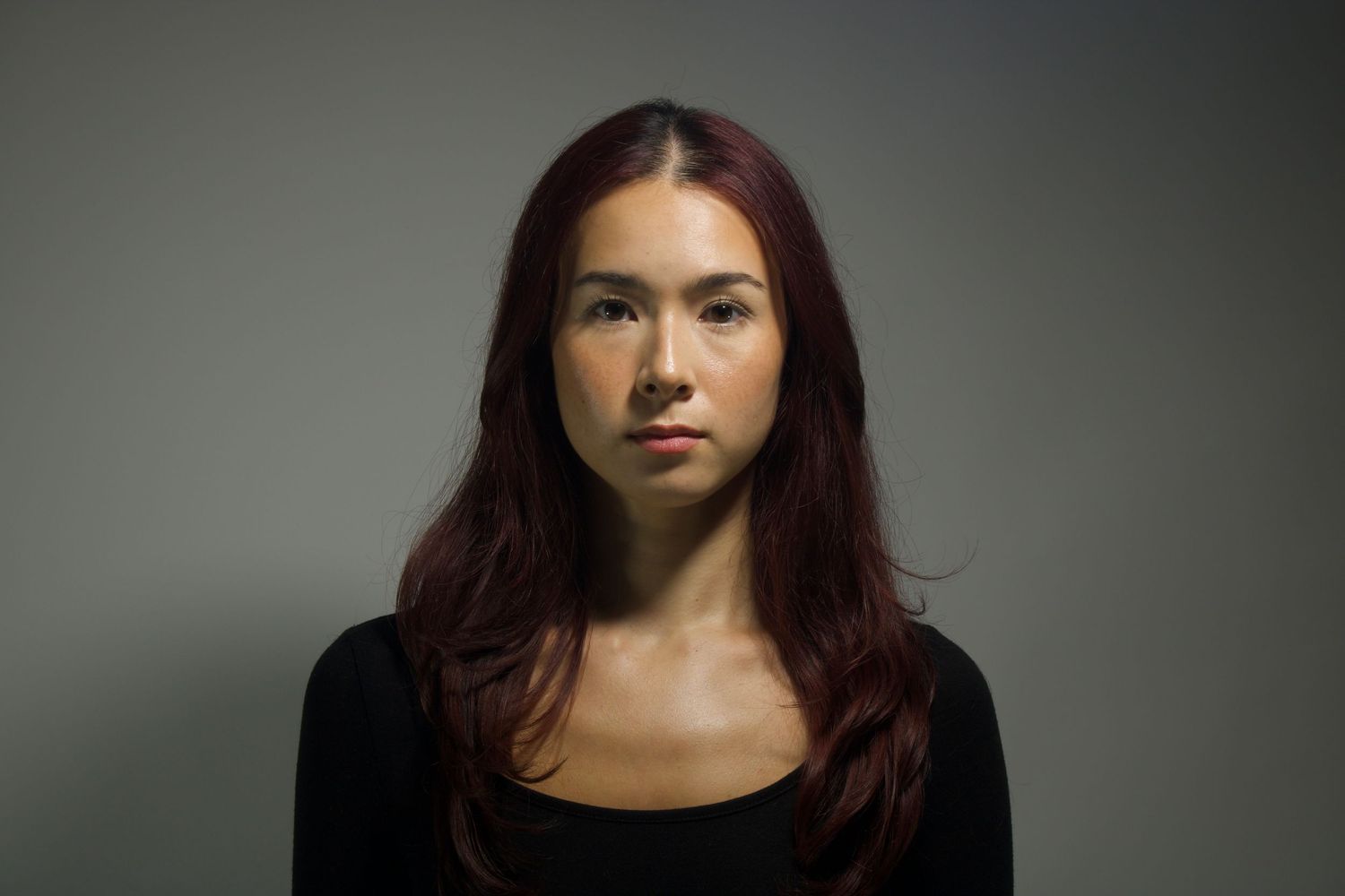 Portrait of a person with burgundy hair against a gray background wearing a black top.