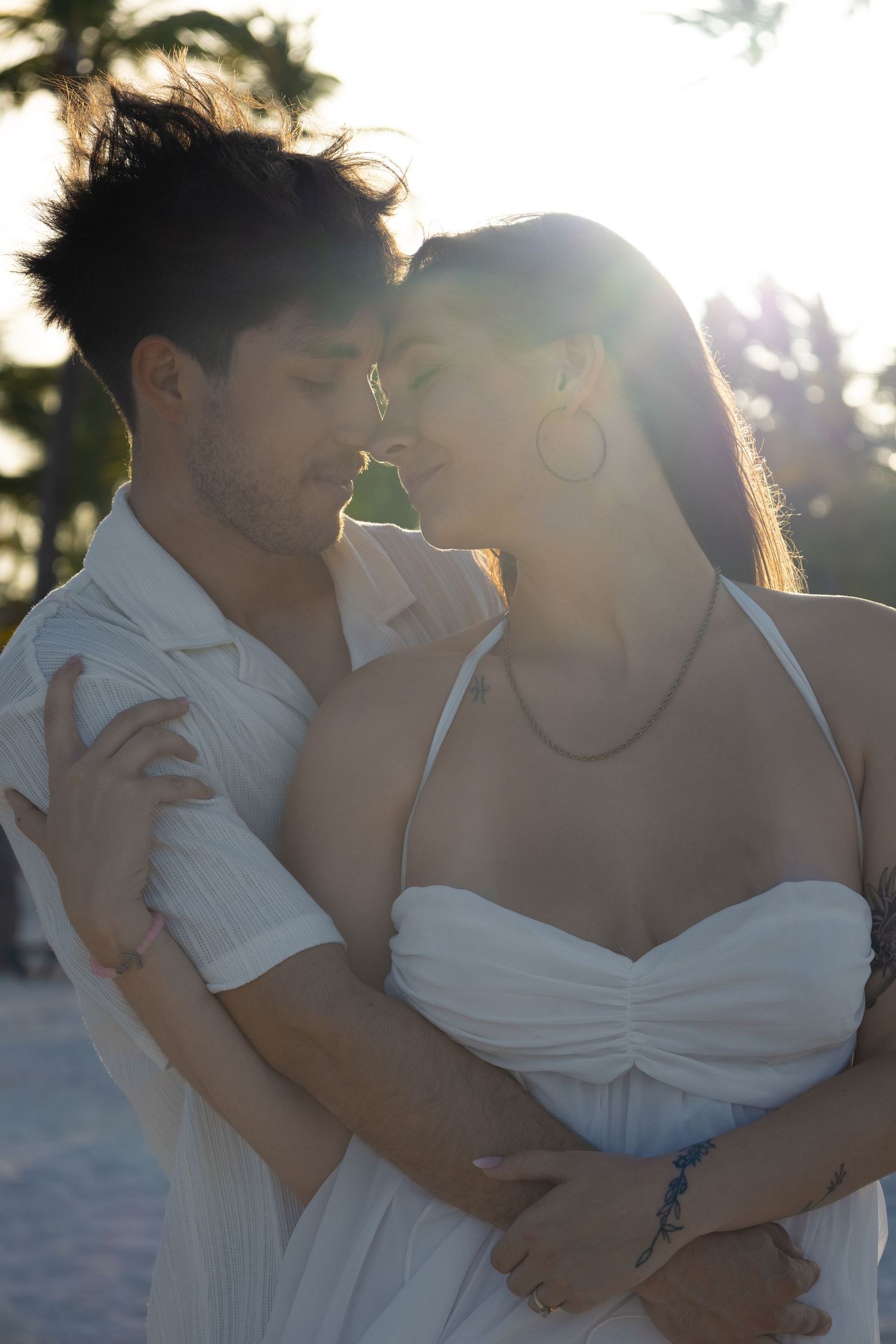 Romantic couple in white embracing at sunset on a tropical beach.