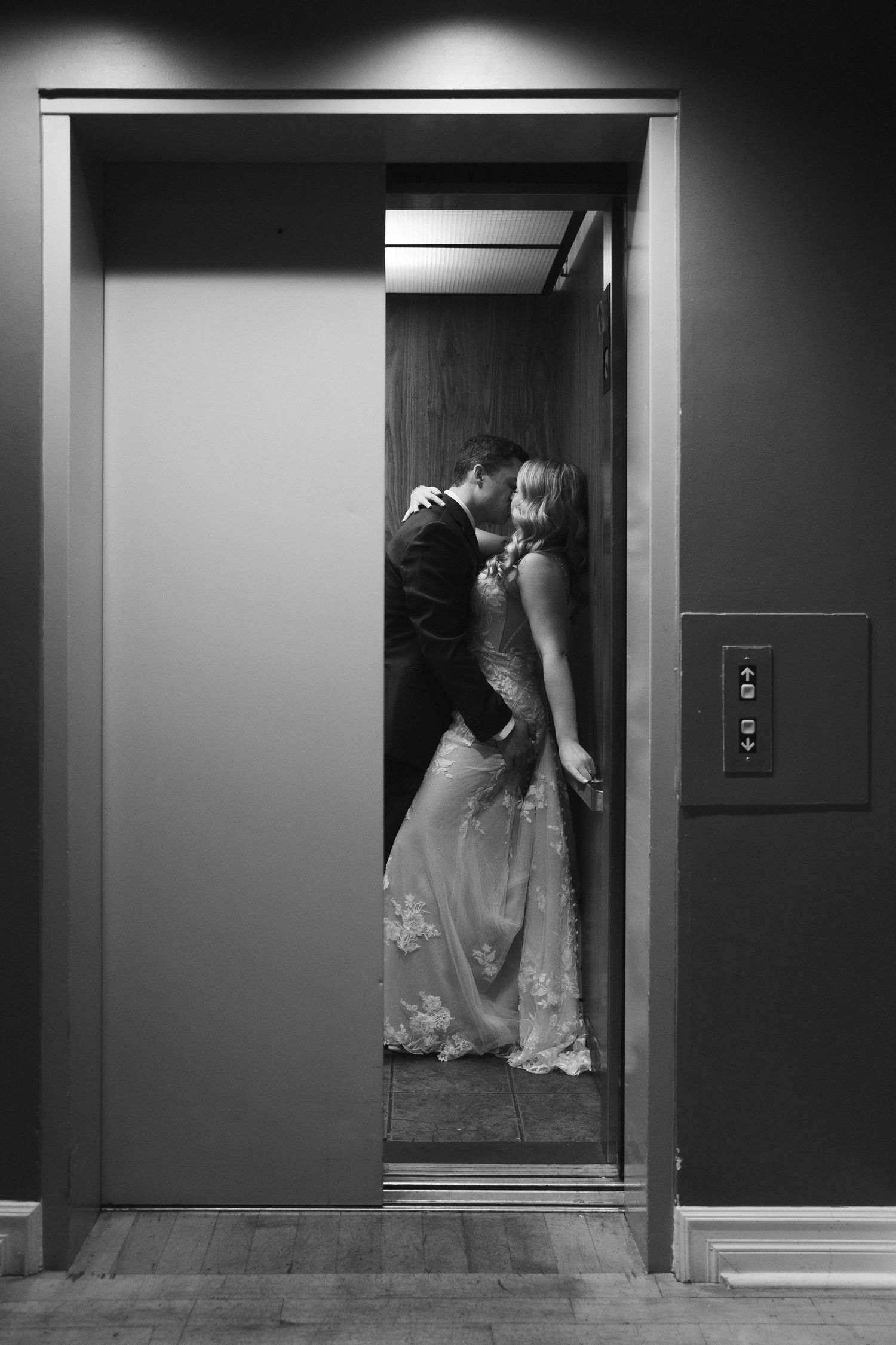 Black and white photo of couple sharing intimate moment in elevator.