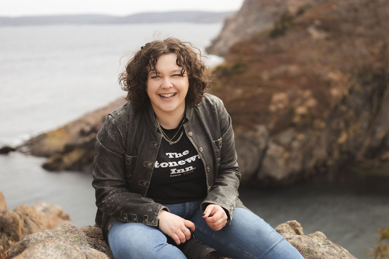 A person sitting on coastal rocks with ocean views in the background.