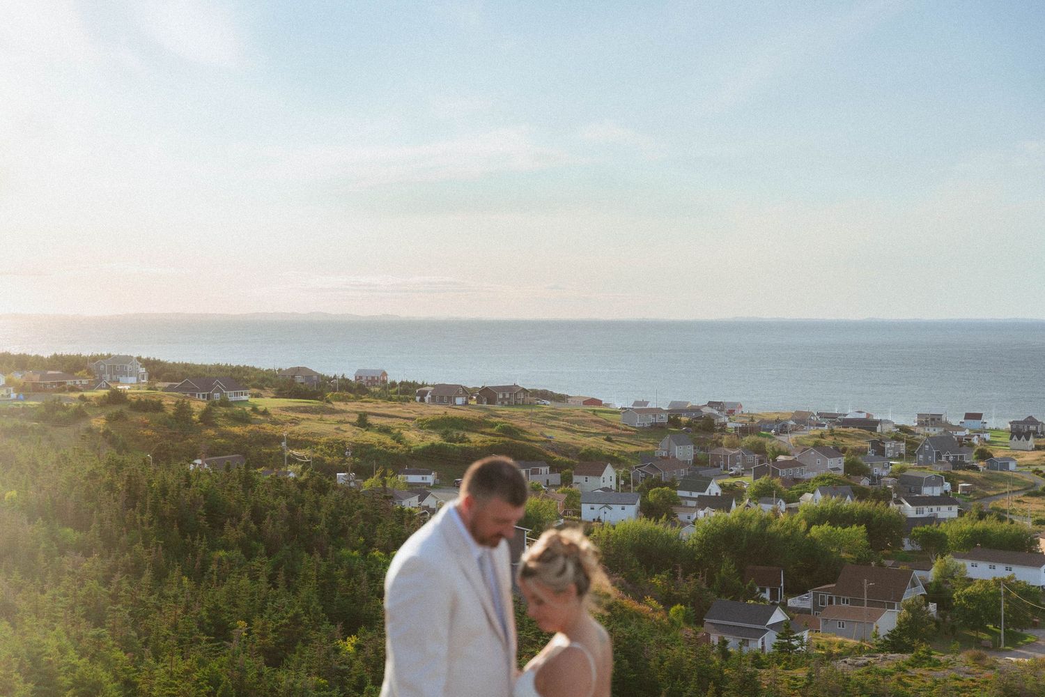 A couple shares a romantic moment overlooking a scenic coastal town with houses dotting the hillside landscape.