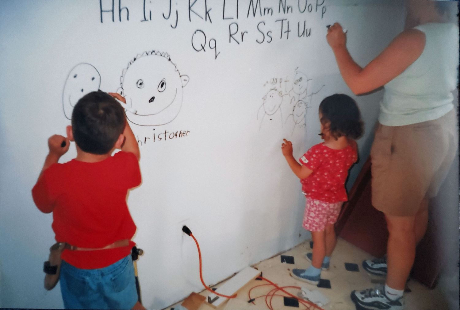Children drawing on a large white wall with letters and doodles.