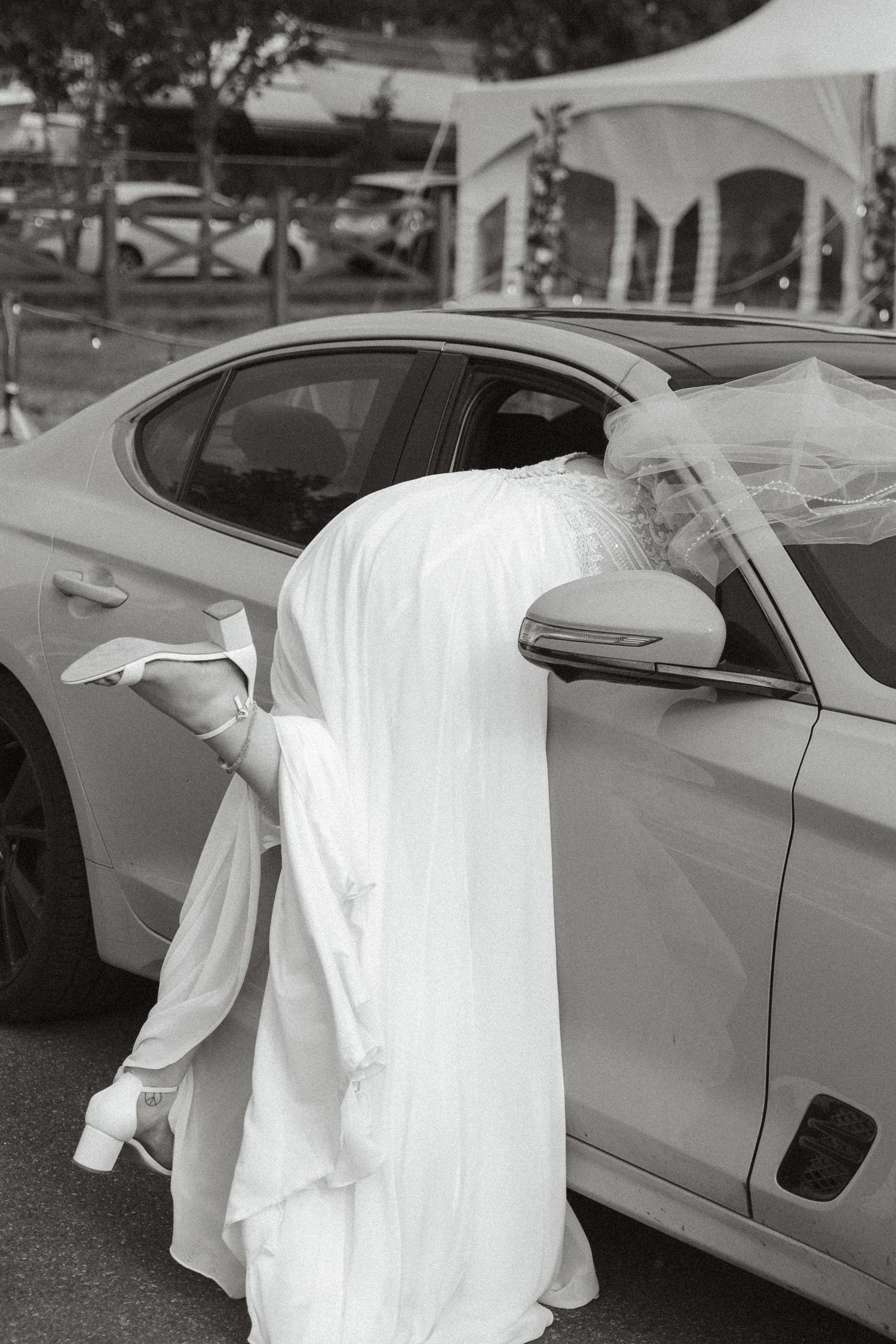 White cloth draped over a silver luxury car in an outdoor parking lot with trees in the background.