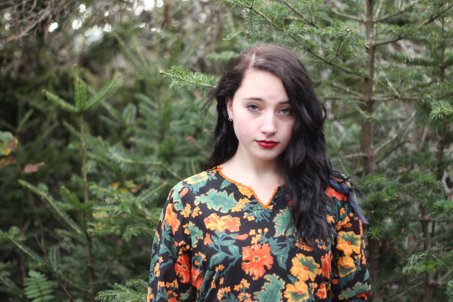 A person in a floral print top stands among green foliage.