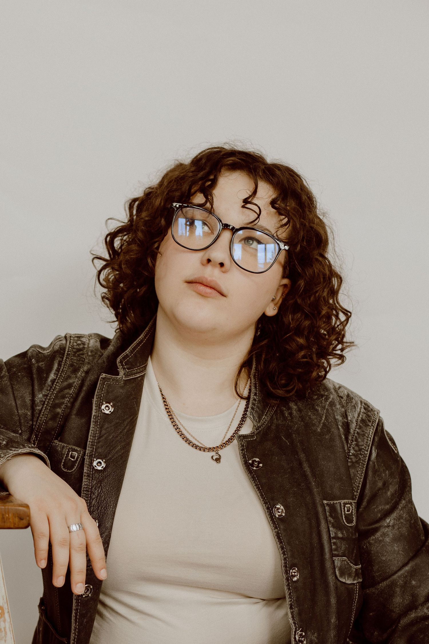 Portrait of person in denim jacket and glasses with curly hair against neutral background.