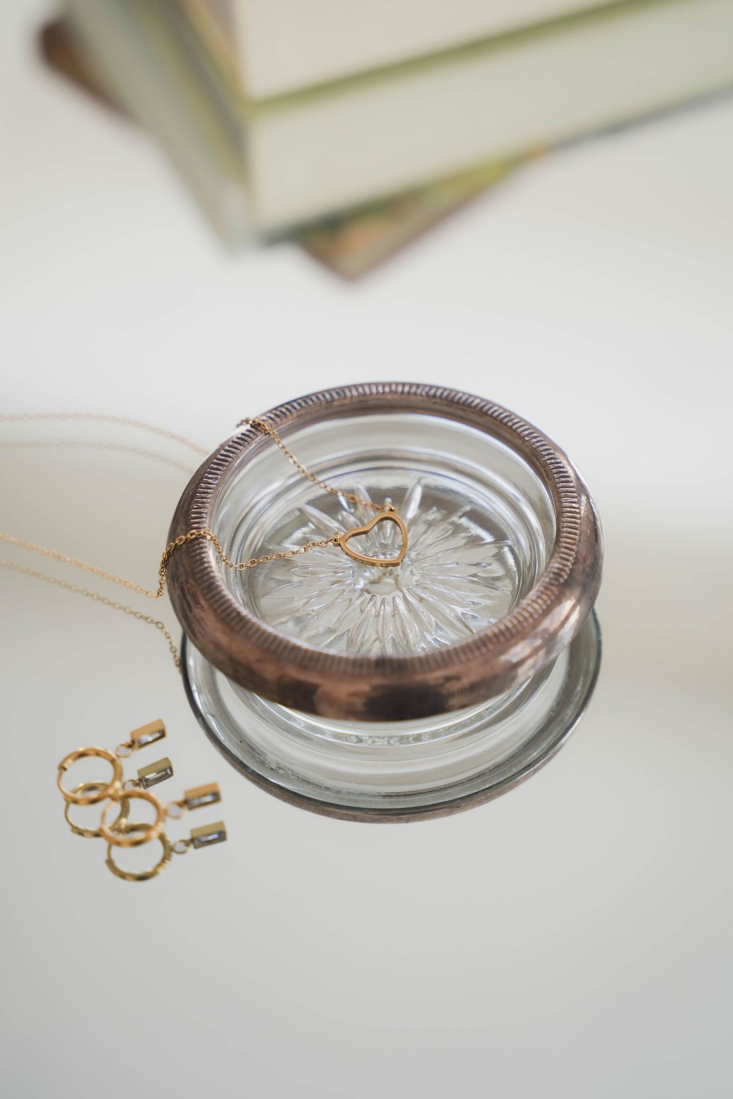 Gold necklace and rings displayed in a vintage glass jar with copper lid on a white surface.