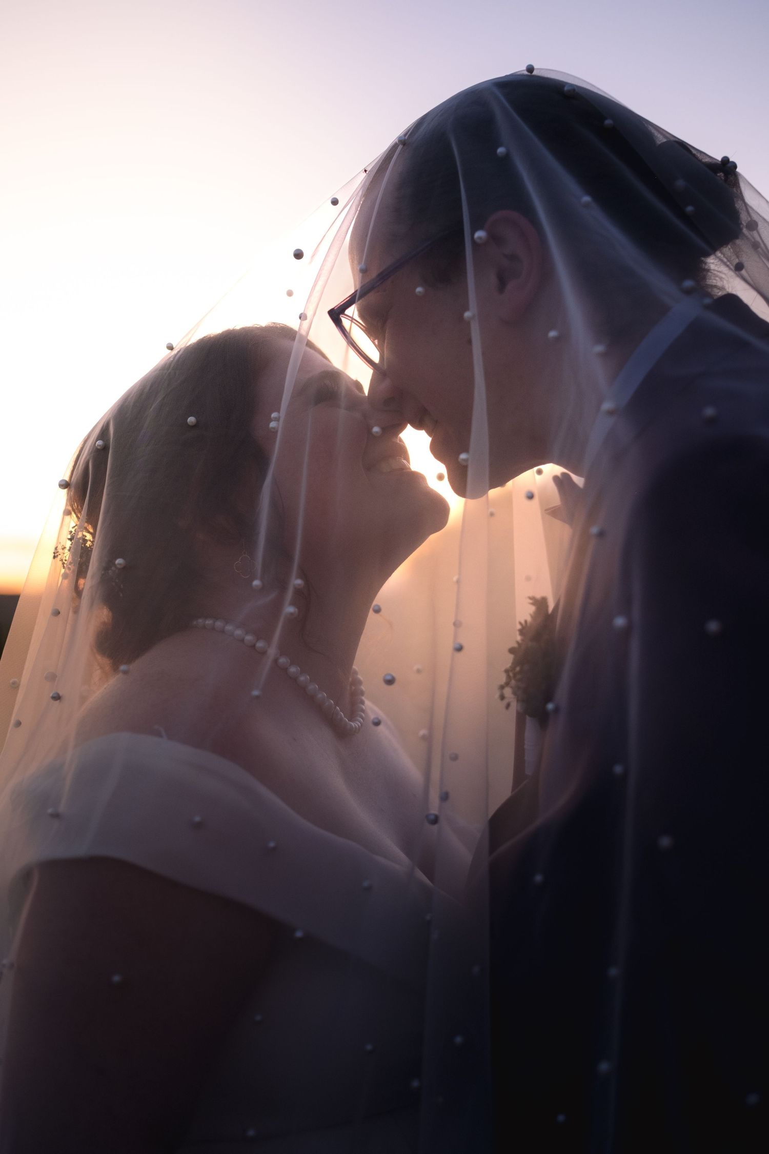 Silhouetted couple shares an intimate moment at sunset through a delicate veil.