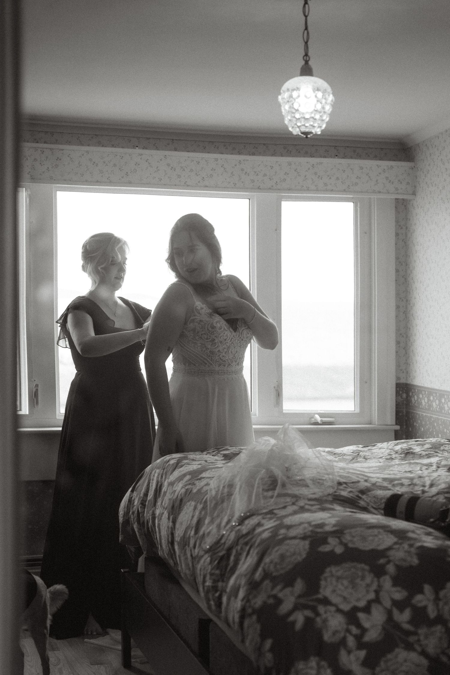 Black and white photo showing a bedroom interior with a crystal chandelier and large windows.