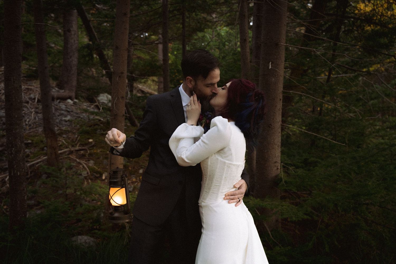 A romantic wedding couple shares an intimate dance in a forest setting with twinkling lights.