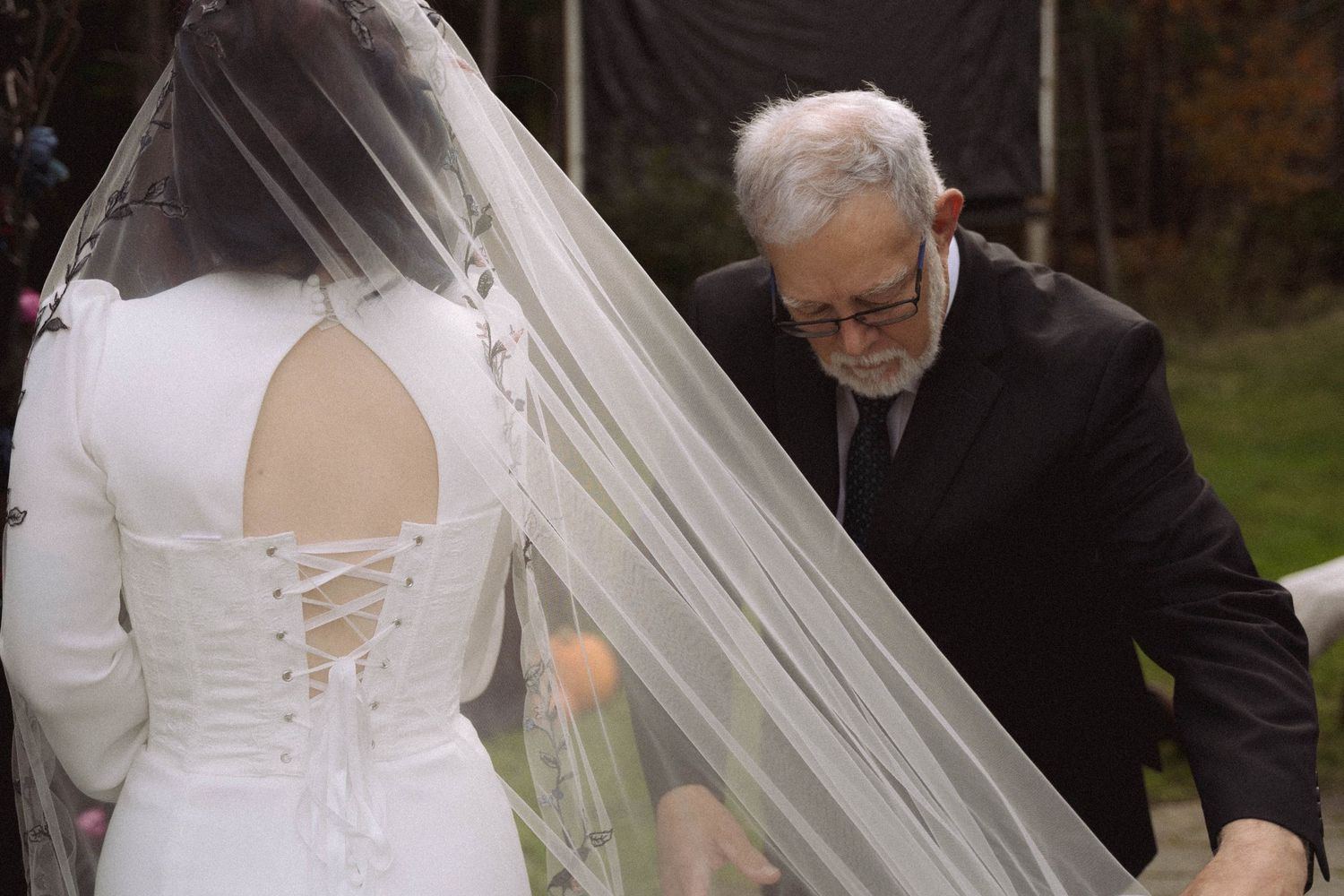 A close-up view of a bride's wedding dress corset back being adjusted during an outdoor ceremony.