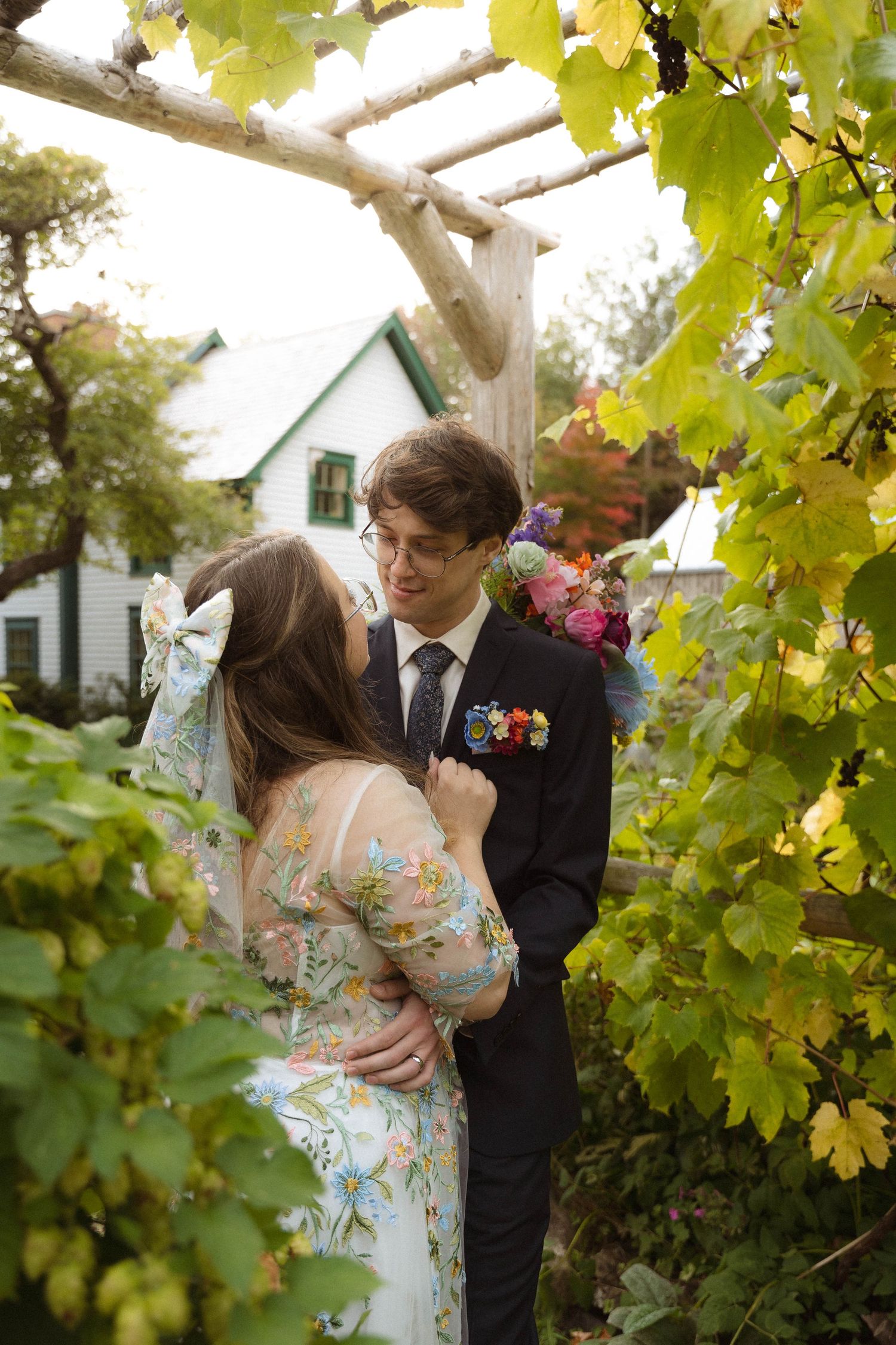 A romantic couple shares an intimate moment under a canopy of yellow autumn leaves in a garden setting.