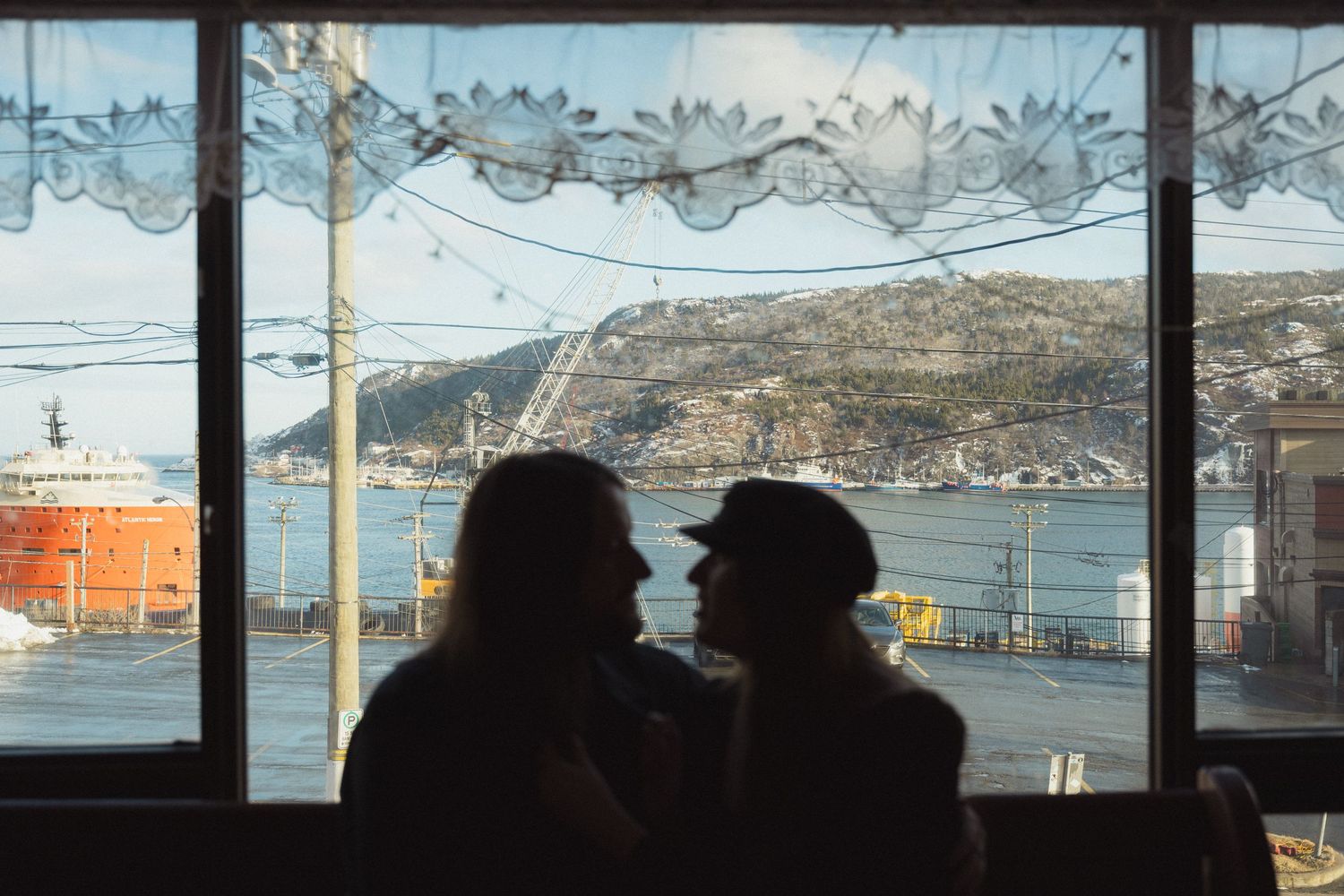 Silhouettes by window with coastal view and decorative lace curtains.