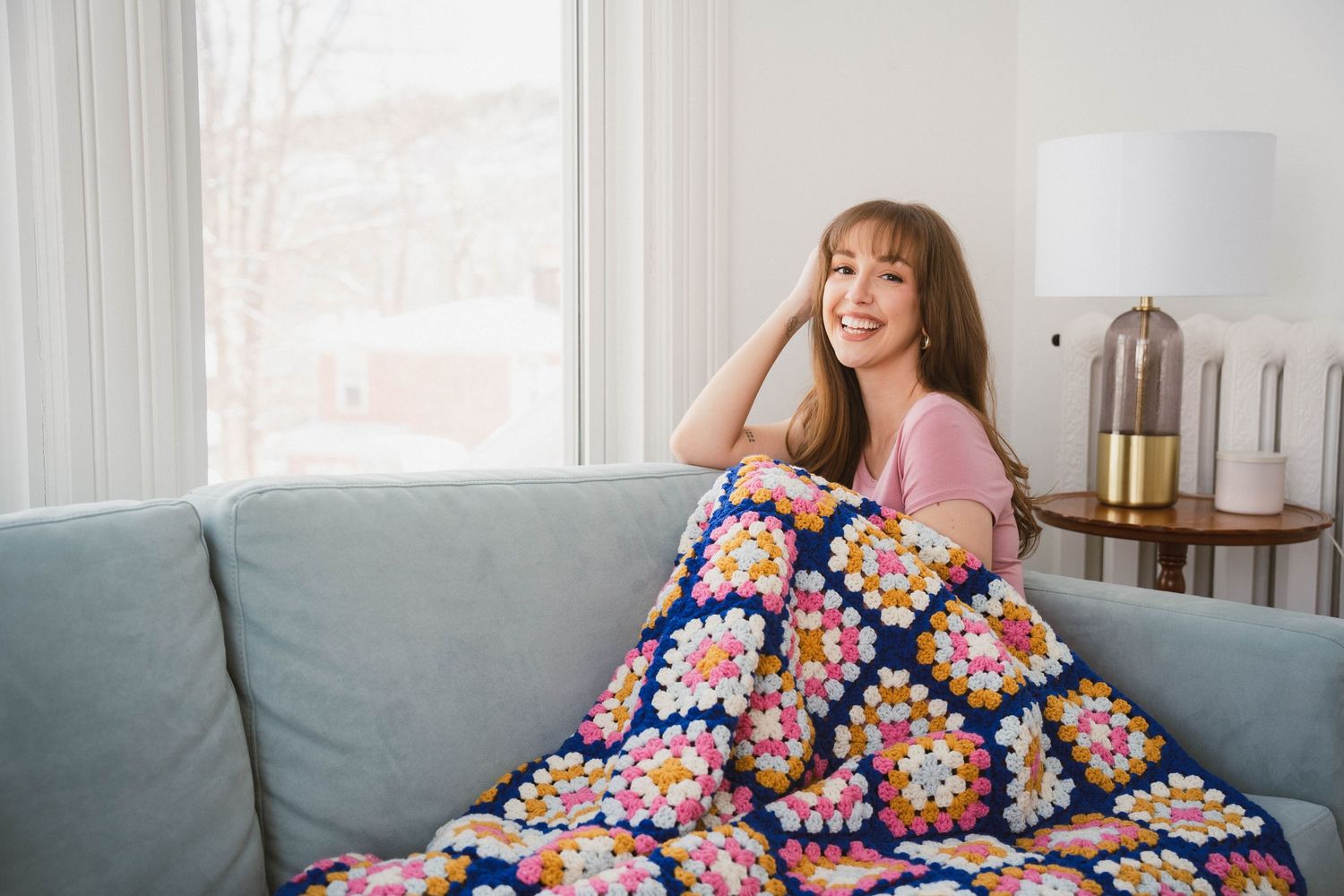 Person relaxing on a couch under a colorful crocheted blanket in a bright, modern living room.