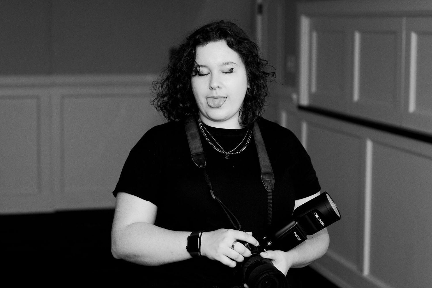A photographer in black clothing holding camera equipment indoors.