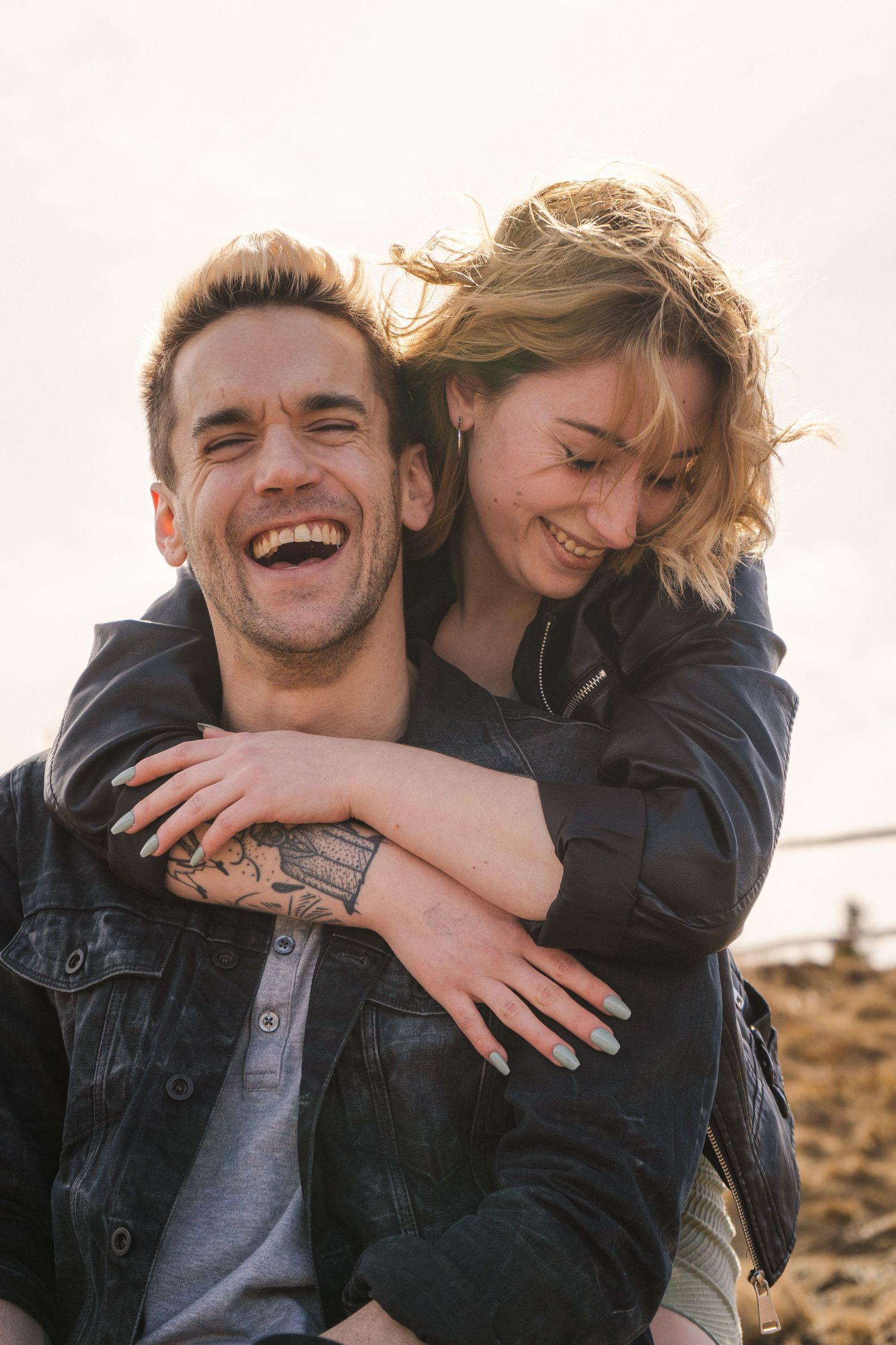 Two people share joyful laughter and hugs in a bright outdoor setting.