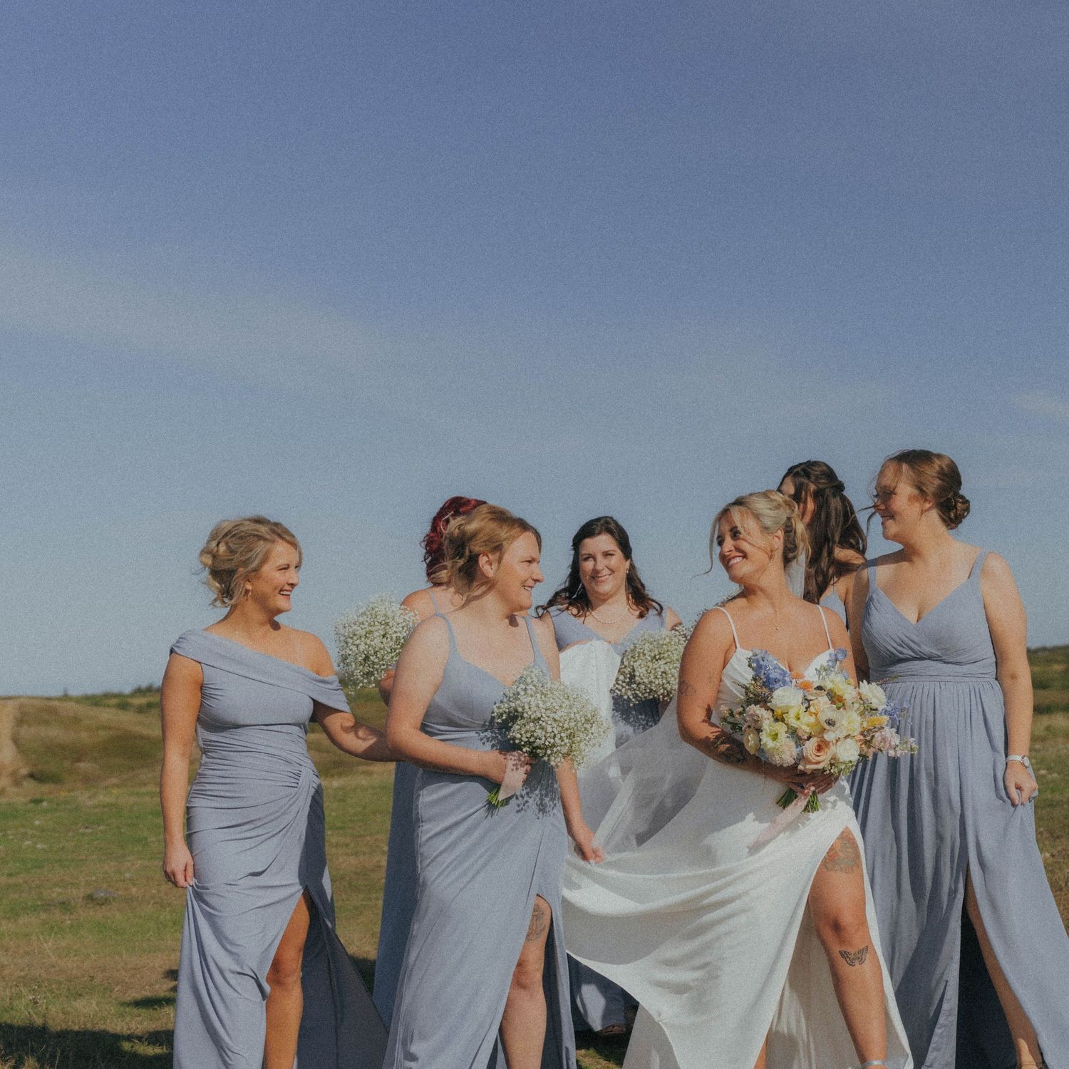 Wedding party in light blue dresses walking together on a hilltop overlooking the ocean.