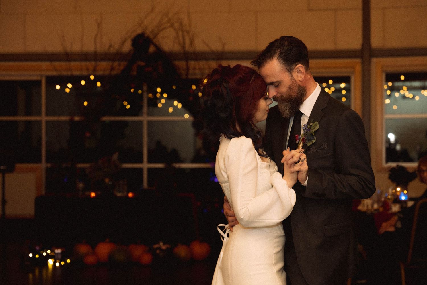 A couple shares their first dance together at an elegant indoor wedding reception with twinkling lights in the background.