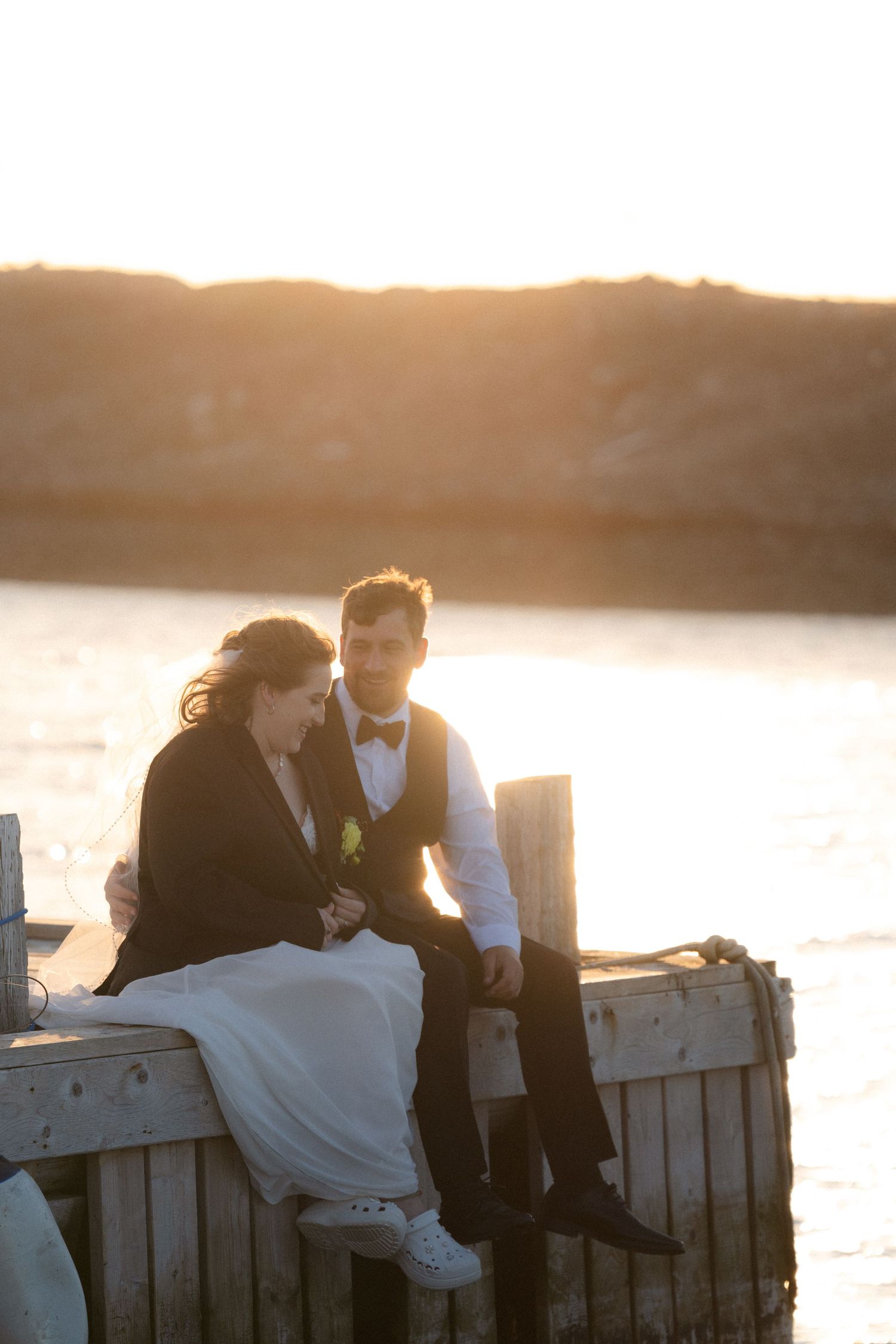 Couple sitting on wooden dock during golden sunset by the water.