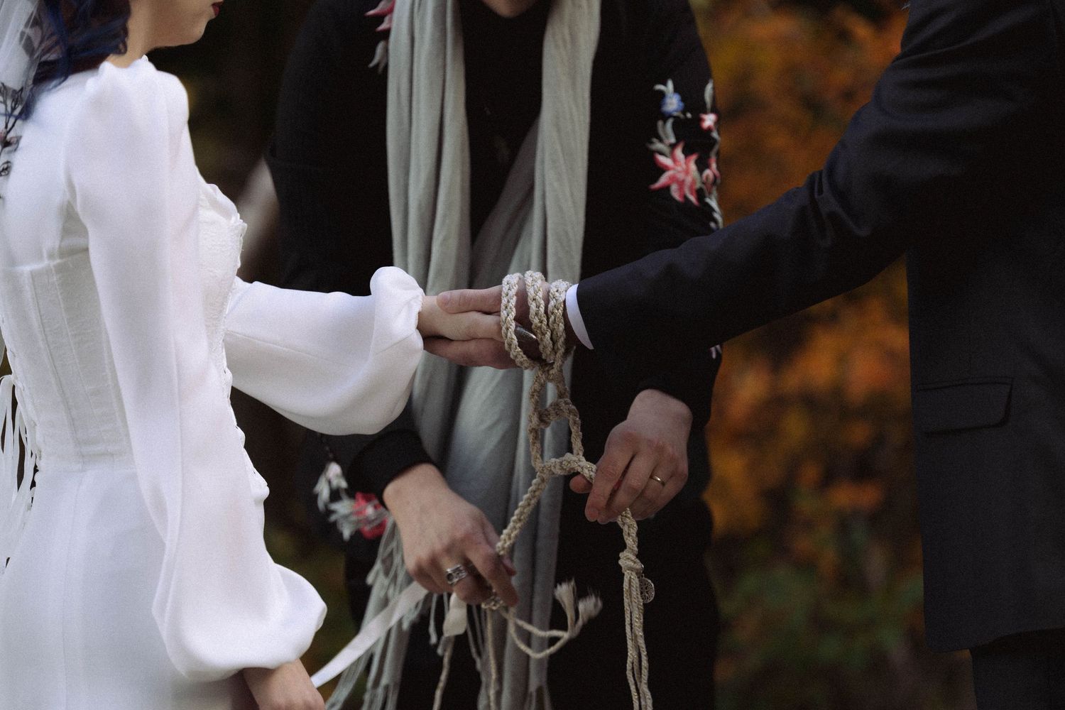 A person in a white dress and black jacket walks down a path surrounded by autumn foliage.