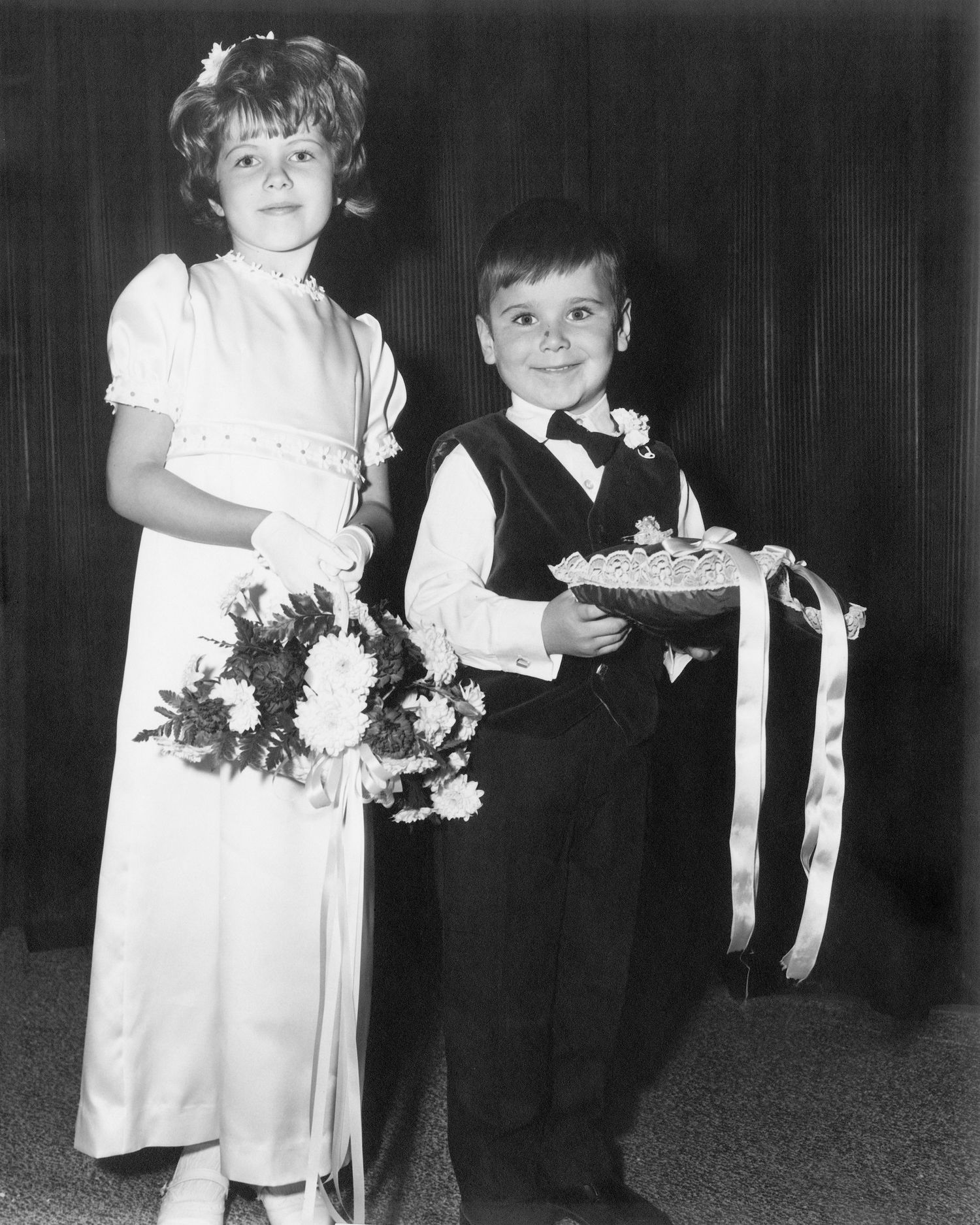 A vintage black and white photograph of two children dressed formally for a wedding ceremony.