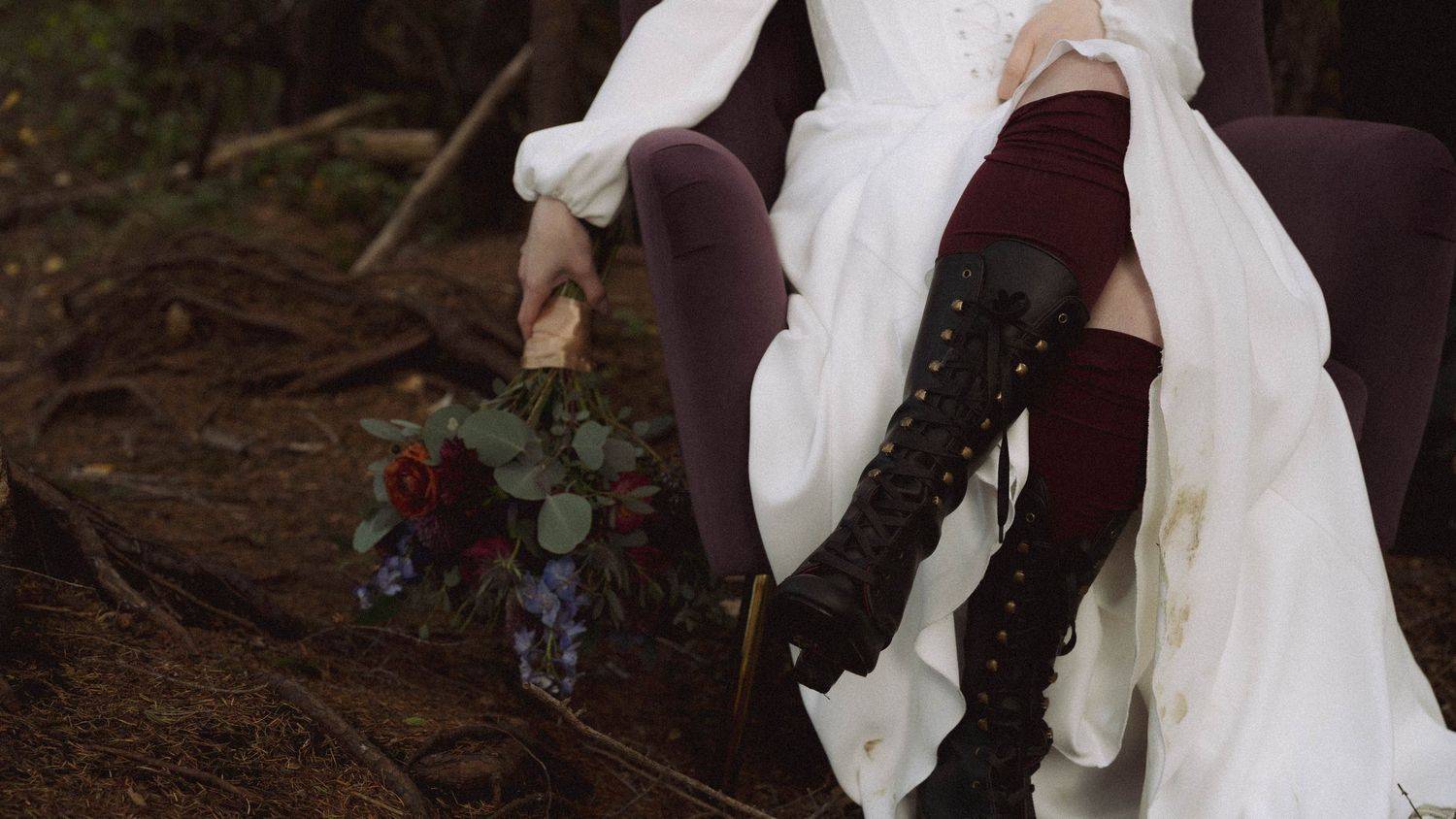 A bride wearing black combat boots with her white wedding dress while sitting on a rustic outdoor bench.