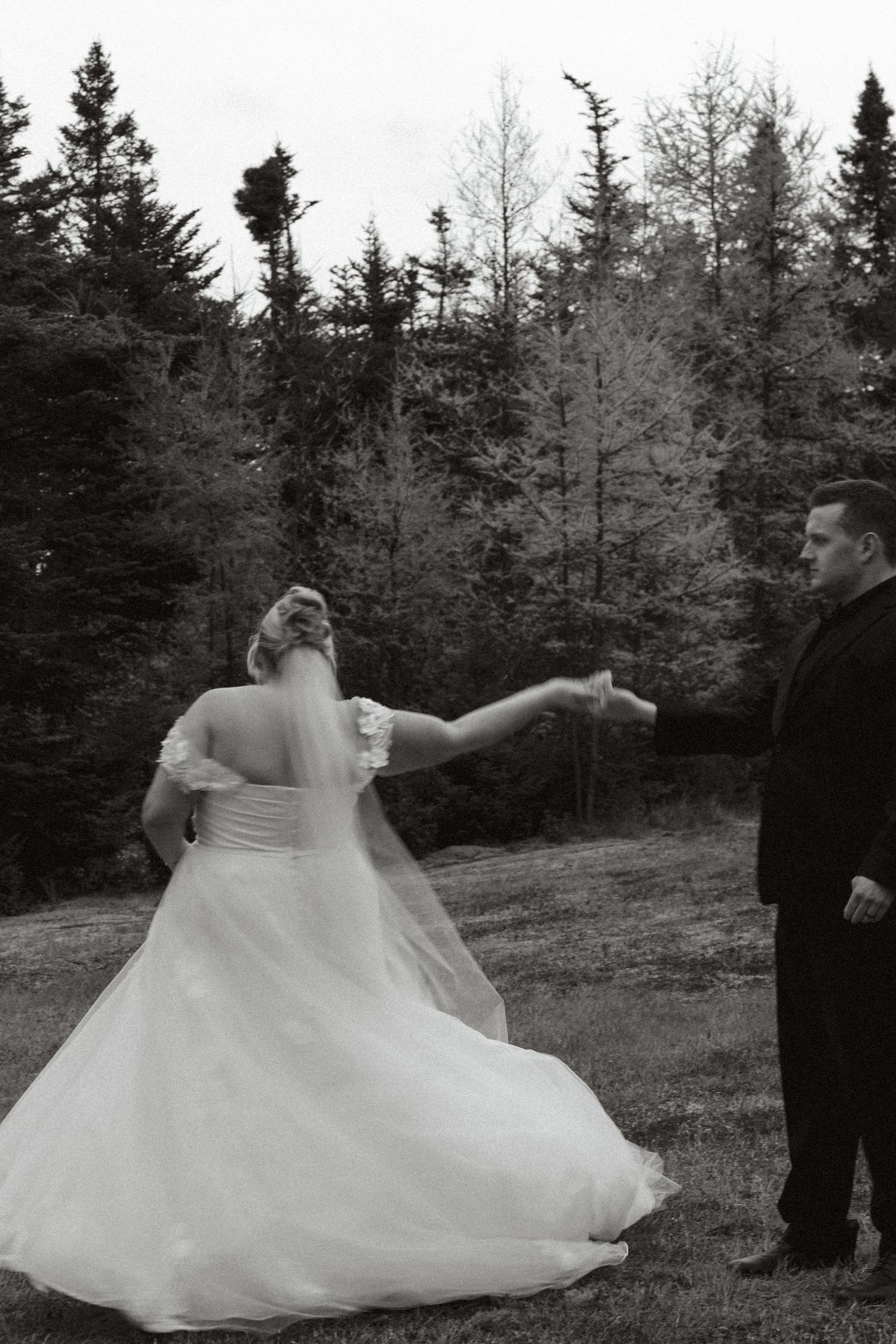 A bride in a flowing white gown twirls gracefully in a forest clearing during a wedding photoshoot.
