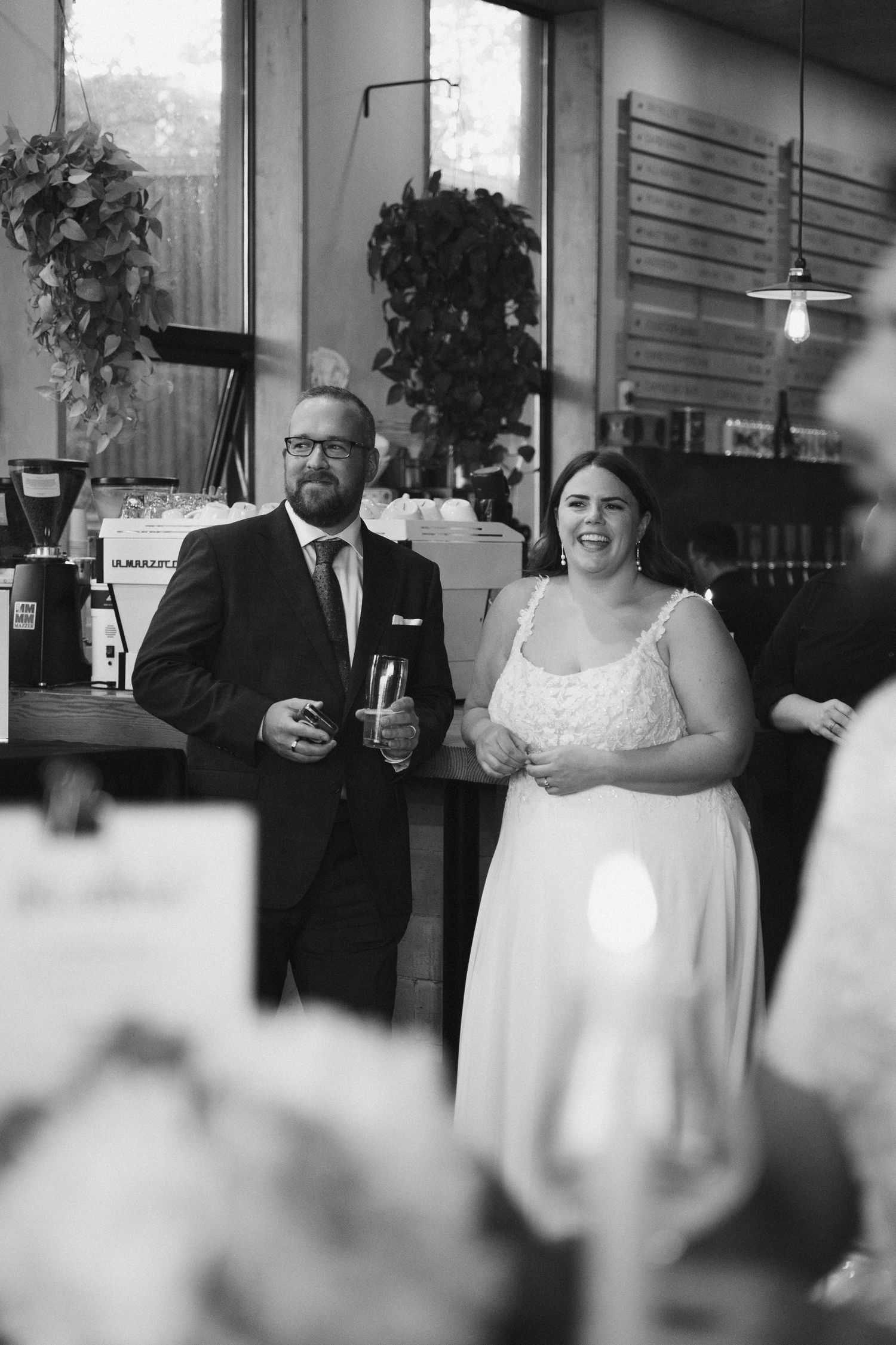 A black and white reception photo of newlyweds sharing drinks and laughter.