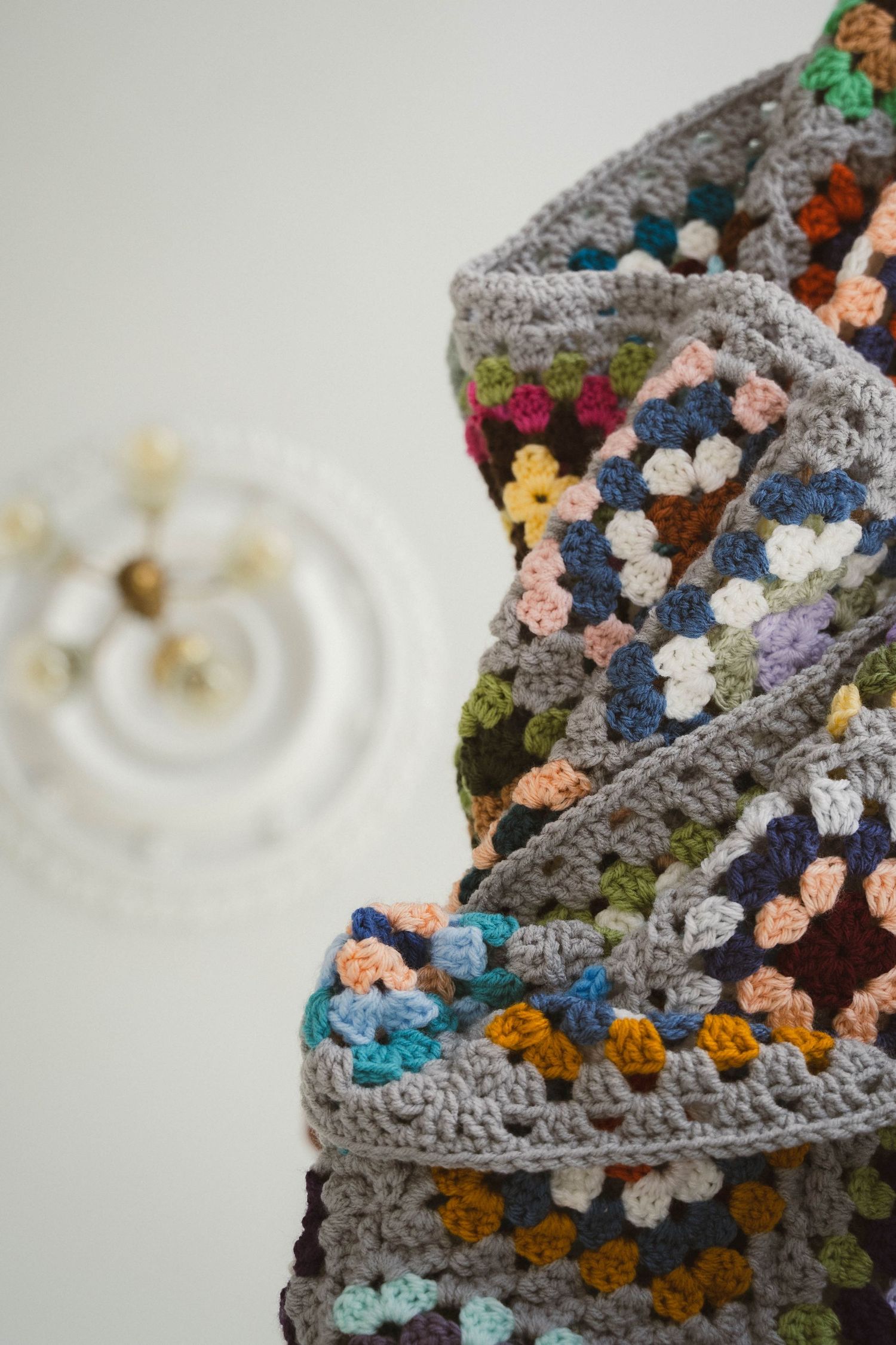 Colorful crocheted granny square blanket with gray border draped over a surface, showcasing multicolor floral motifs.