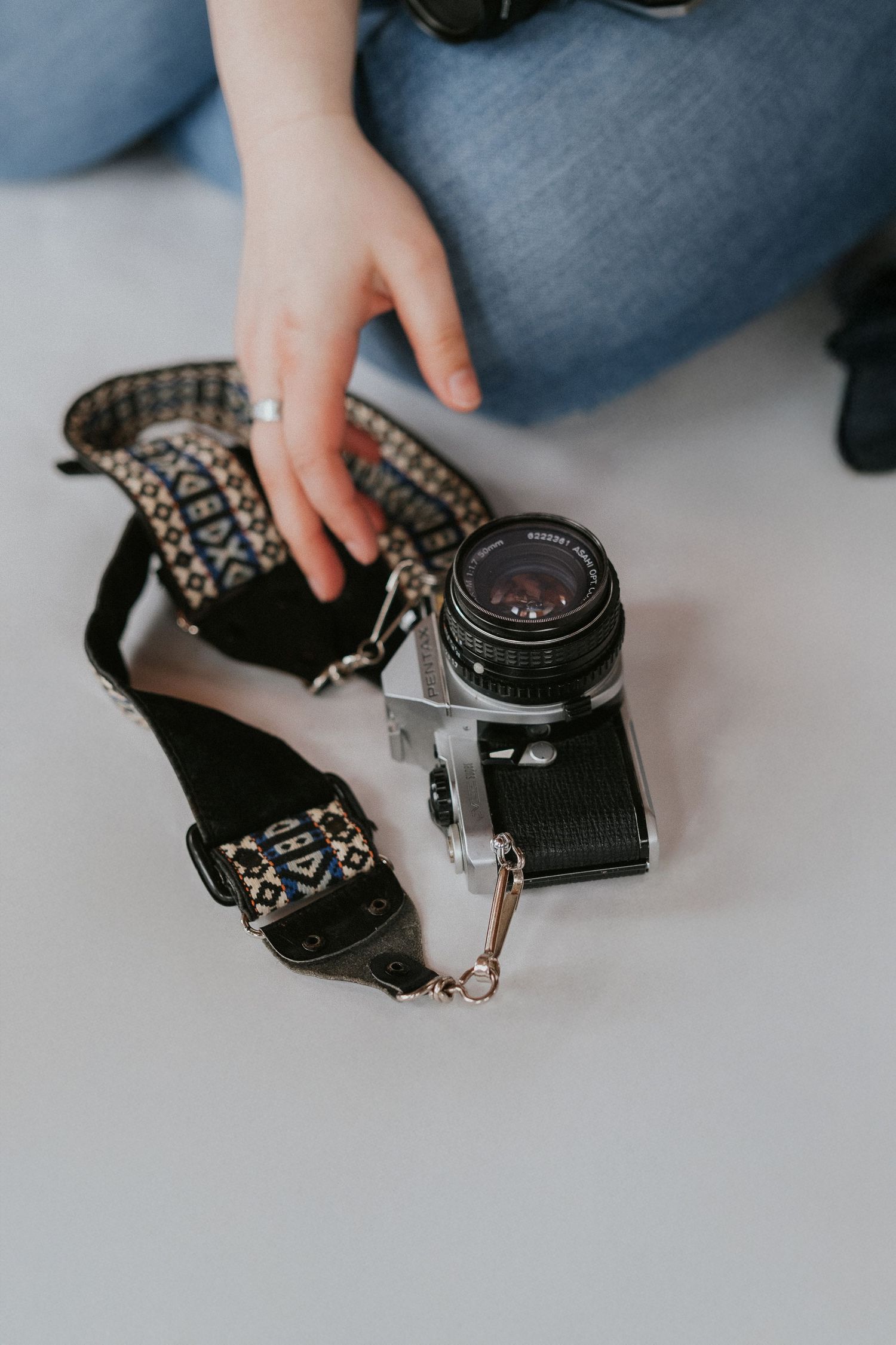 Hands holding and examining a vintage camera with decorative strap on white surface.