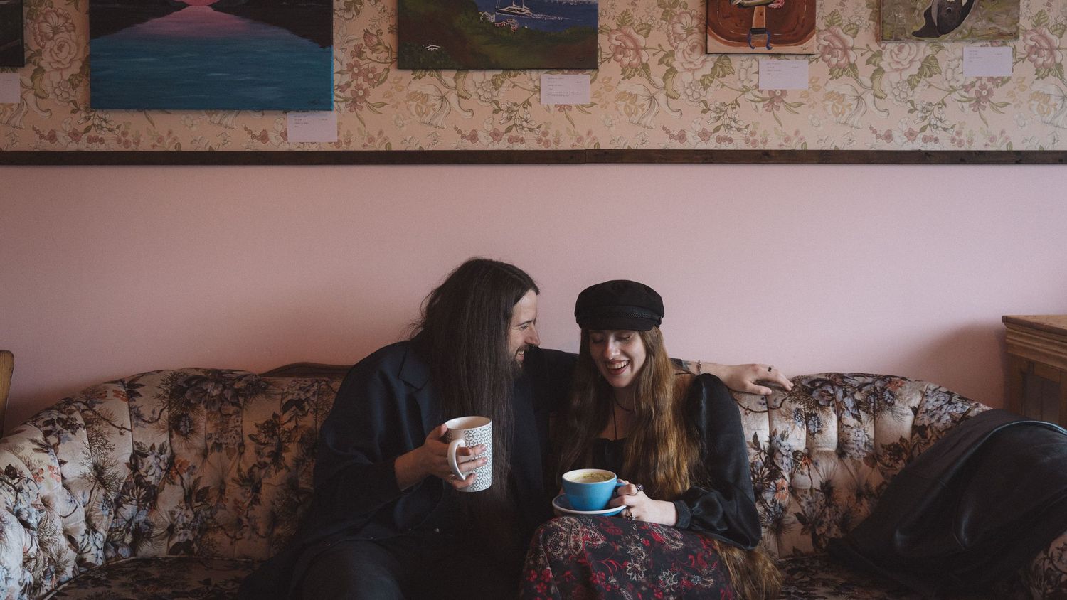 Two friends sharing coffee and conversation on a vintage floral couch.