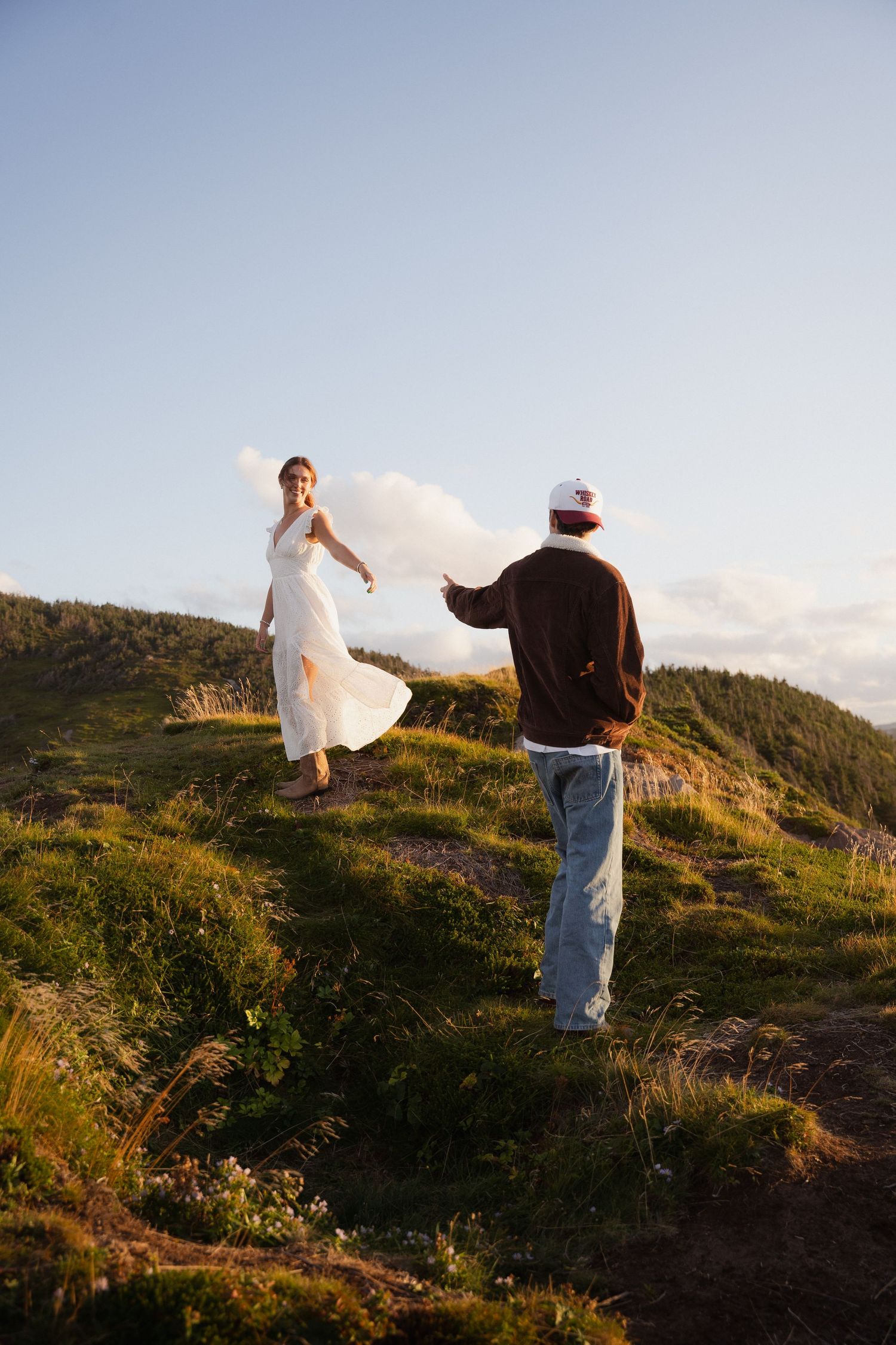Two people walking on a grassy hilltop against a bright blue sky.