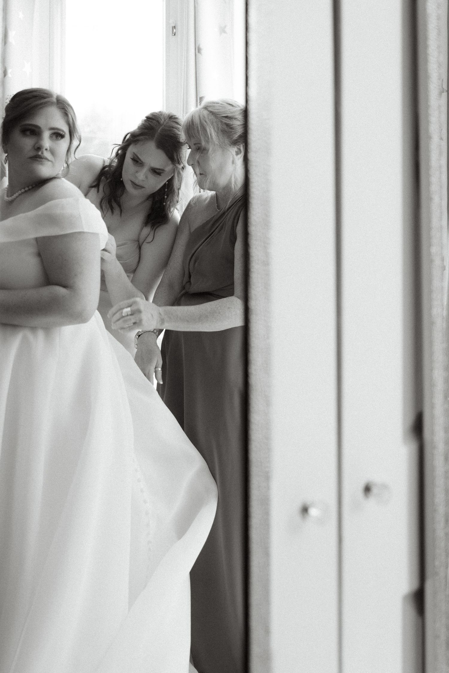 A black and white image showing bridesmaids in formal dresses standing in front of white columns.