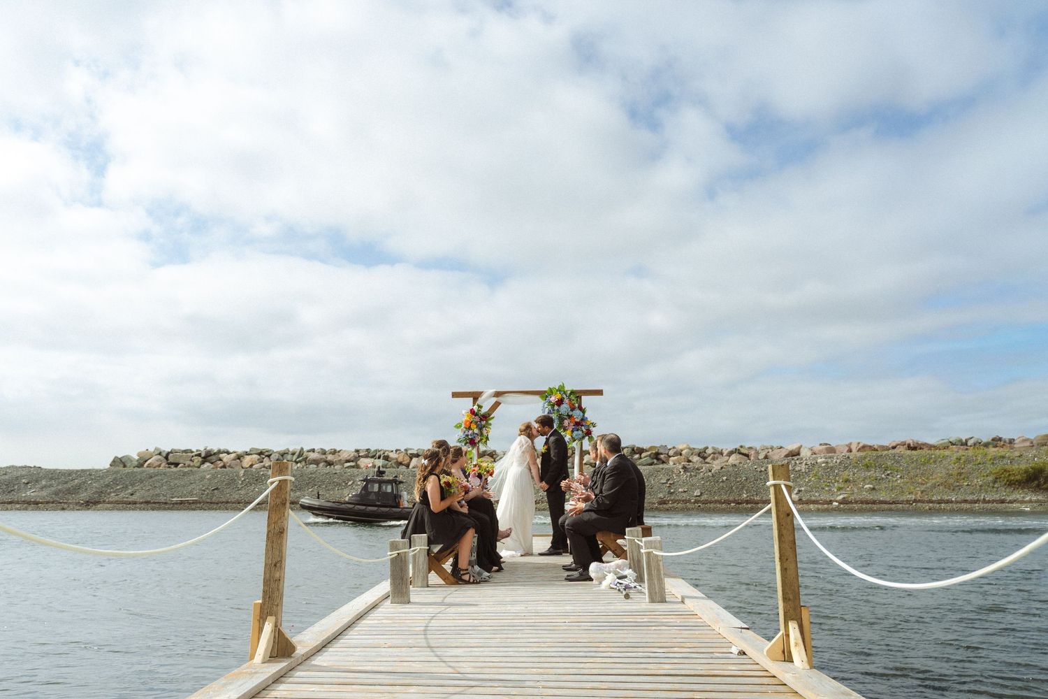 Wooden boardwalk leading to the ocean under cloudy skies with people walking in the distance.